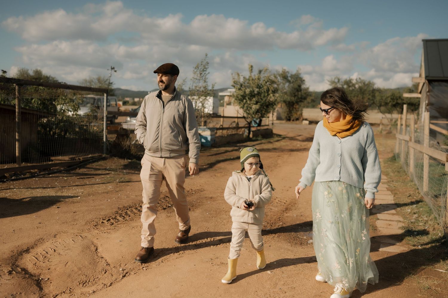 A family takes a stroll together on a dirt path under cloudy skies at a rural property.