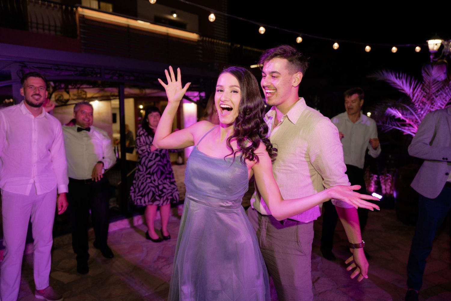 People dancing and celebrating at a lively wedding reception with purple lighting and a festive atmosphere.
