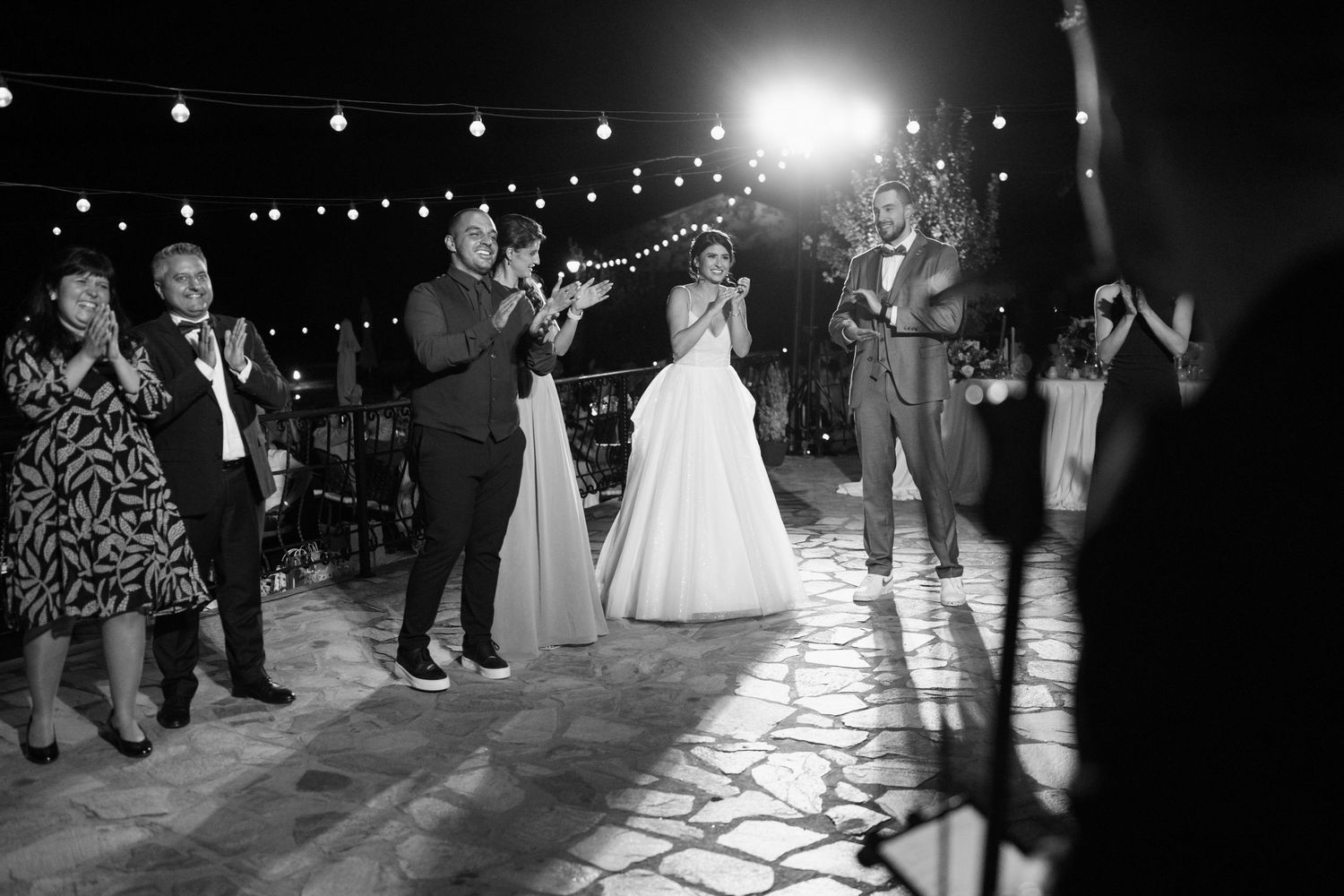 Black and white photo of couples dancing at a wedding reception under string lights and glowing ambiance.