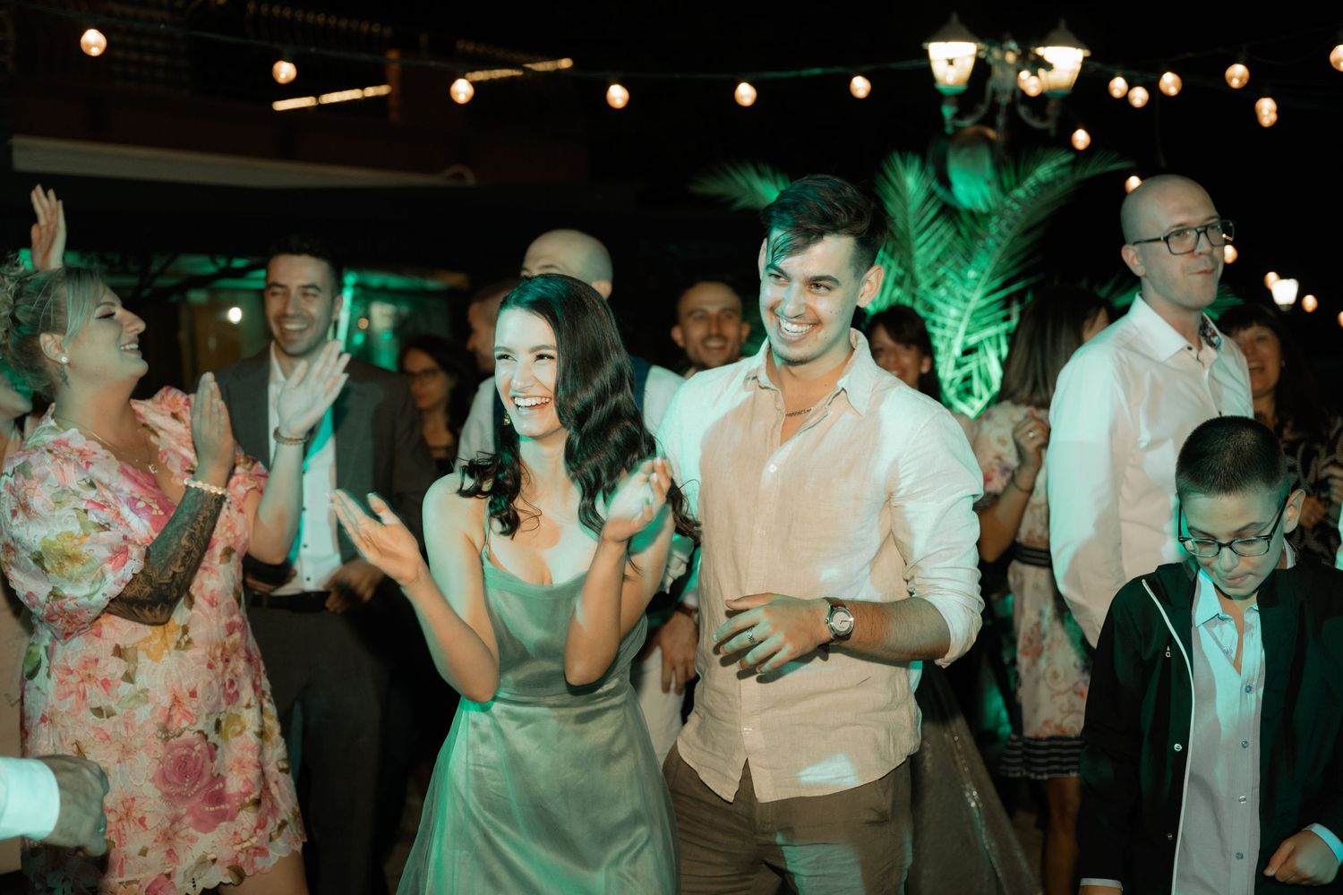 People dancing and celebrating at a nighttime wedding reception with festive lighting and decorations.