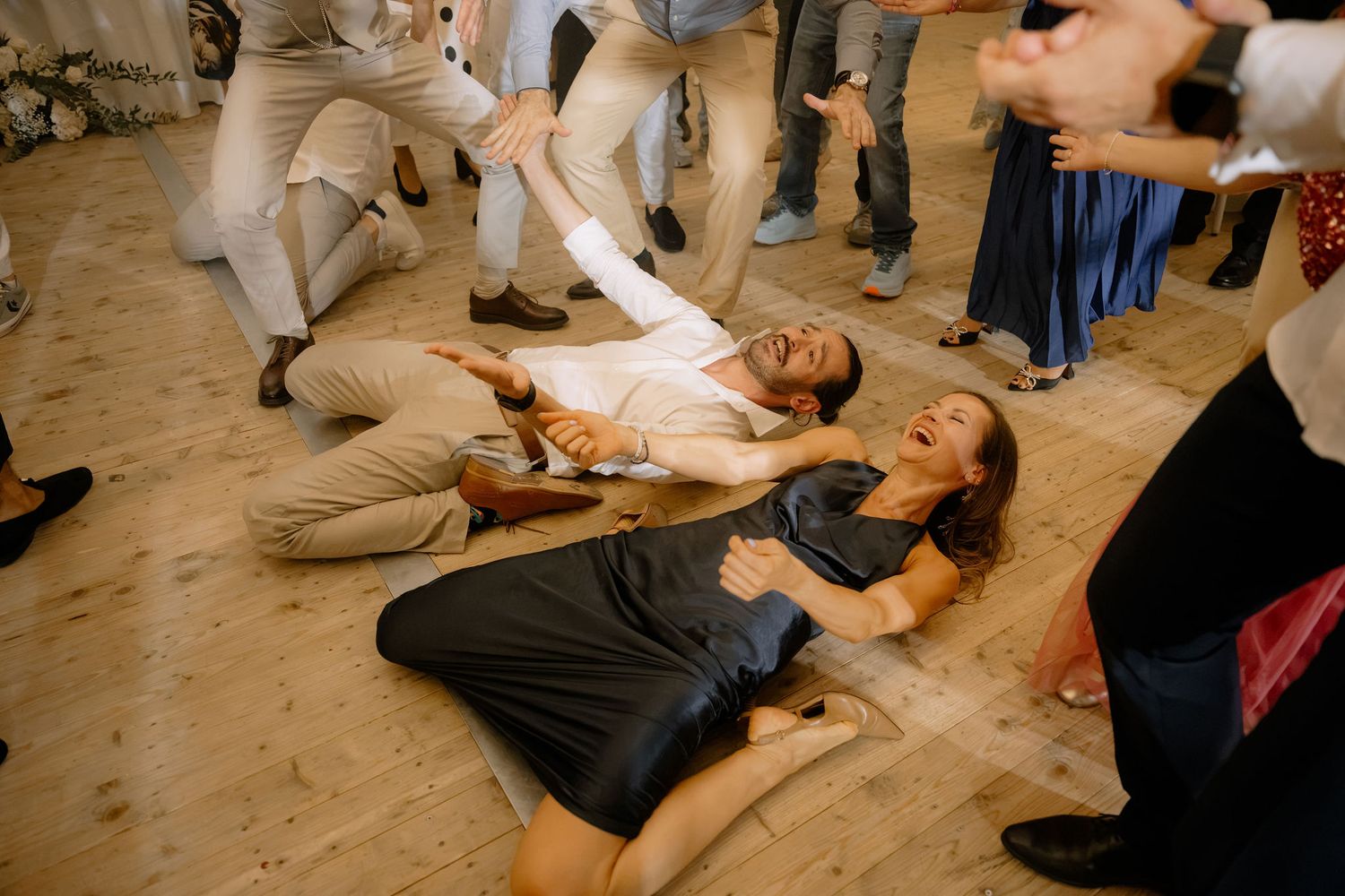 Two wedding guests laughing and lying on the dance floor during a lively wedding reception celebration.