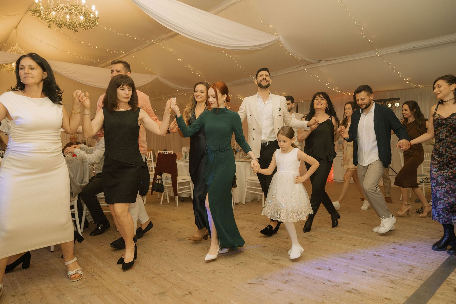 Group of elegantly dressed guests dancing together at a wedding reception in a decorated venue.