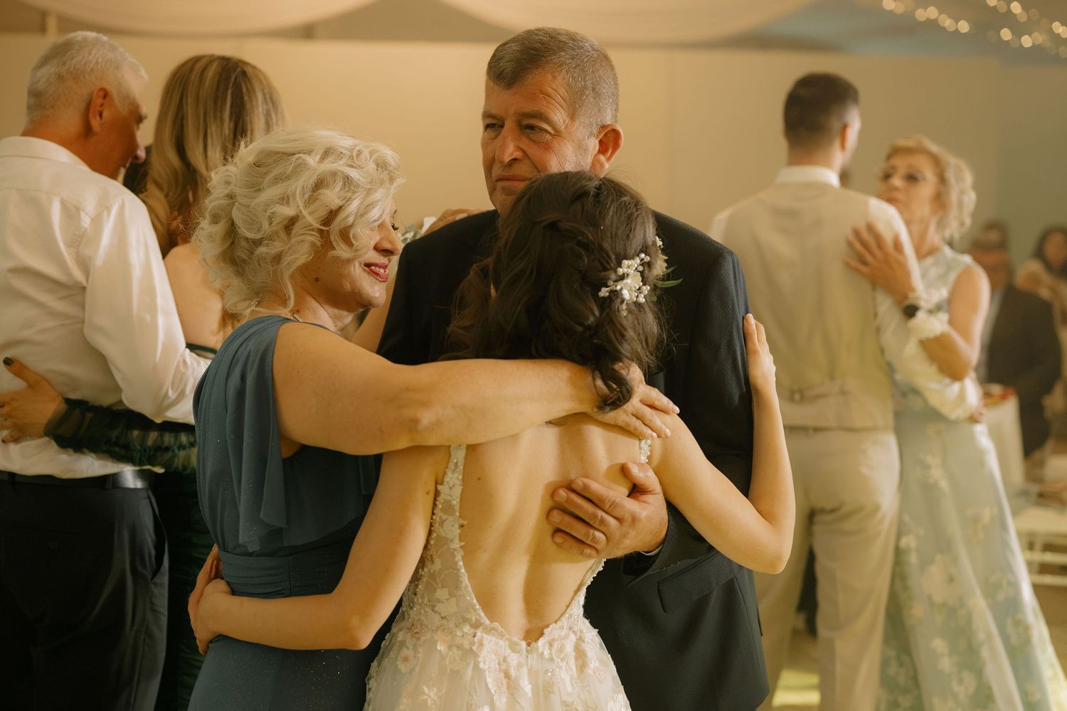 Bride embracing parents in an emotional group hug on the wedding dance floor during reception celebration.