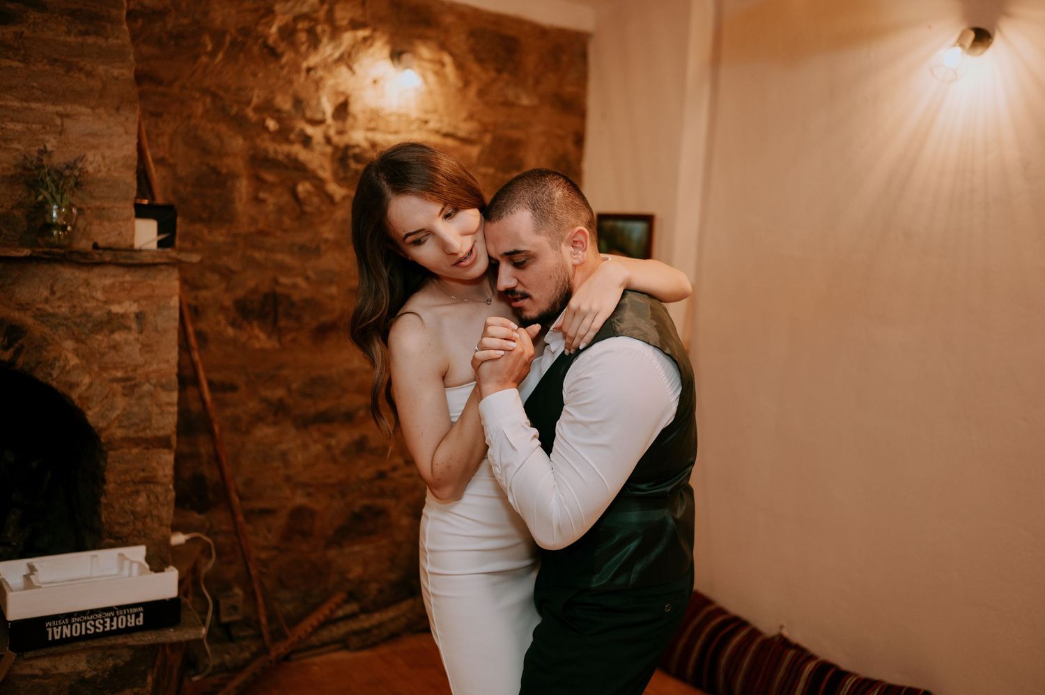 Dancers embrace in an intimate setting with rustic stone walls and soft lighting.