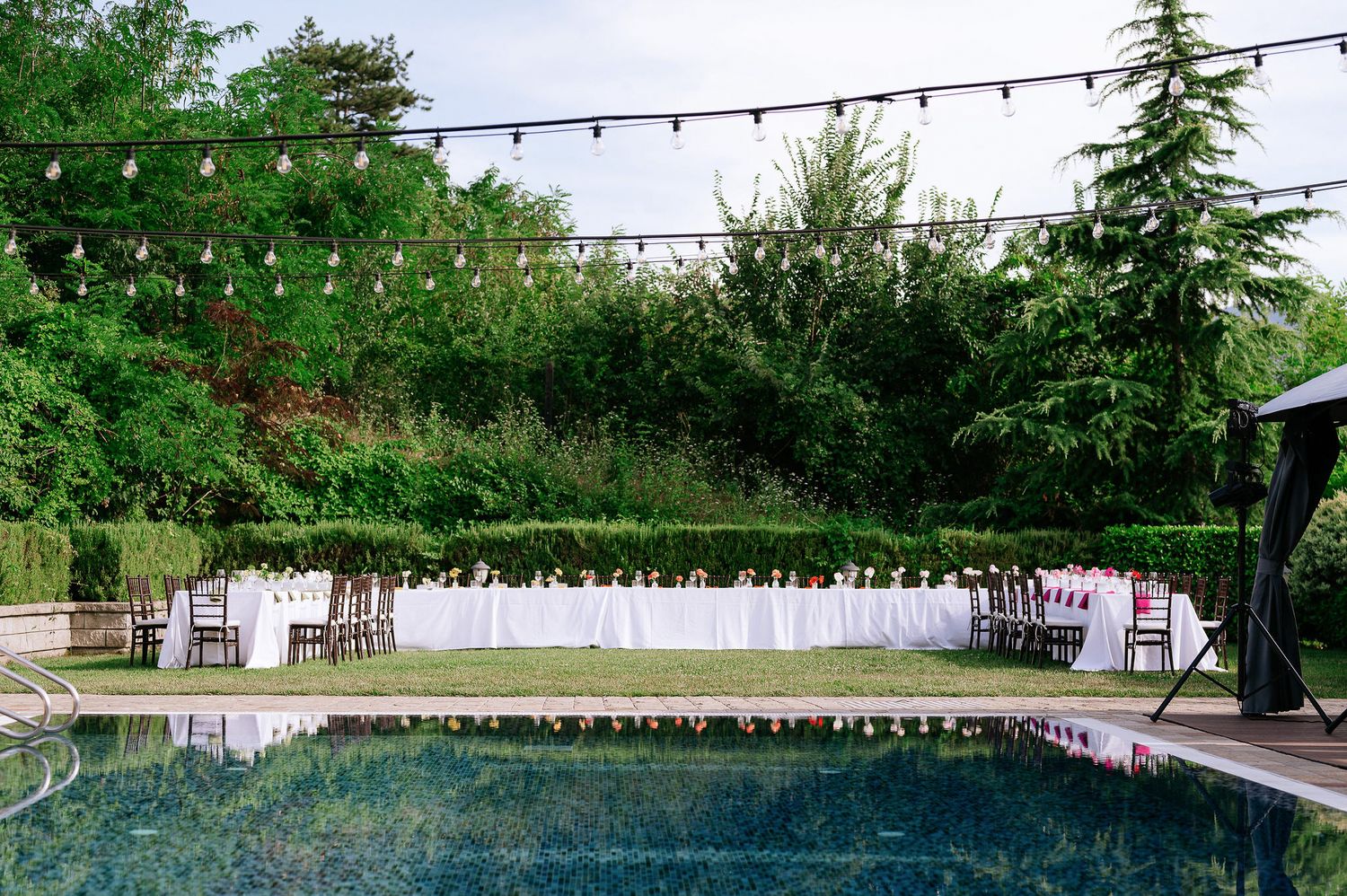 Panoramic view of an outdoor event space with string lights and rows of tables set for a celebration.