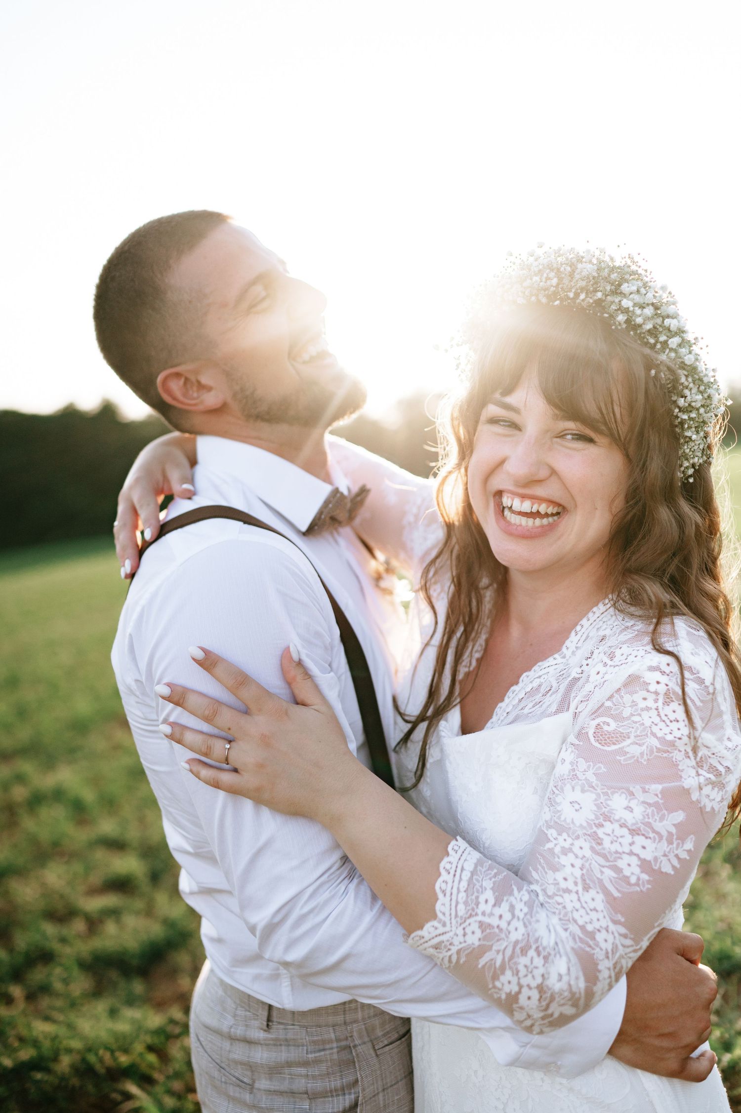 Sun-drenched wedding portrait captures couple's genuine laughter in outdoor setting.