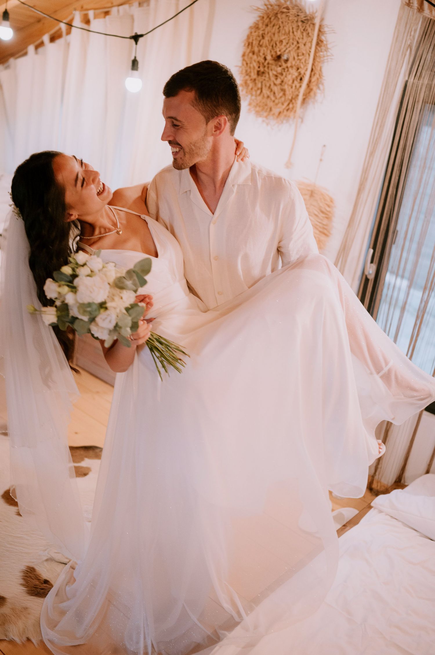 A couple sharing an intimate moment in a bright white room with hanging macrame decorations.
