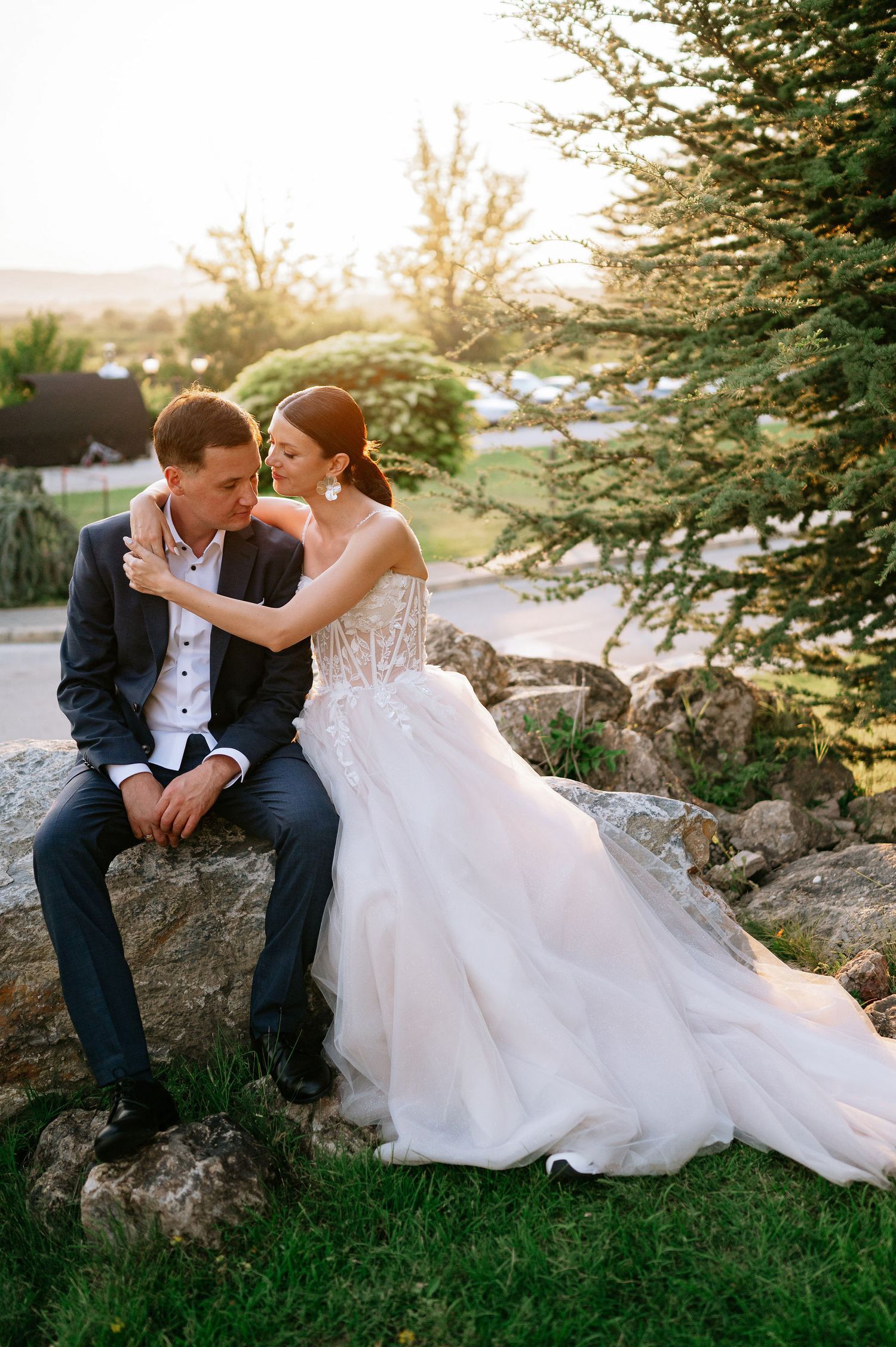 Sunset wedding portrait of couple relaxing on decorative garden rocks.