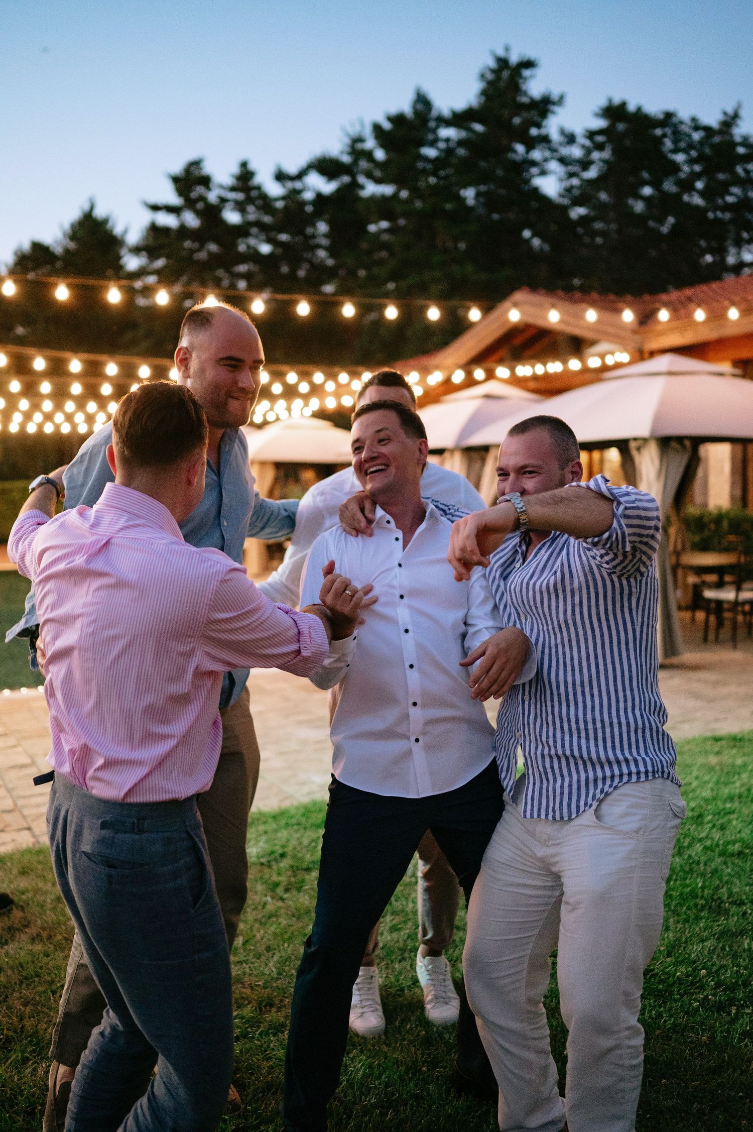 Friends embracing and laughing during a festive outdoor party at sunset.