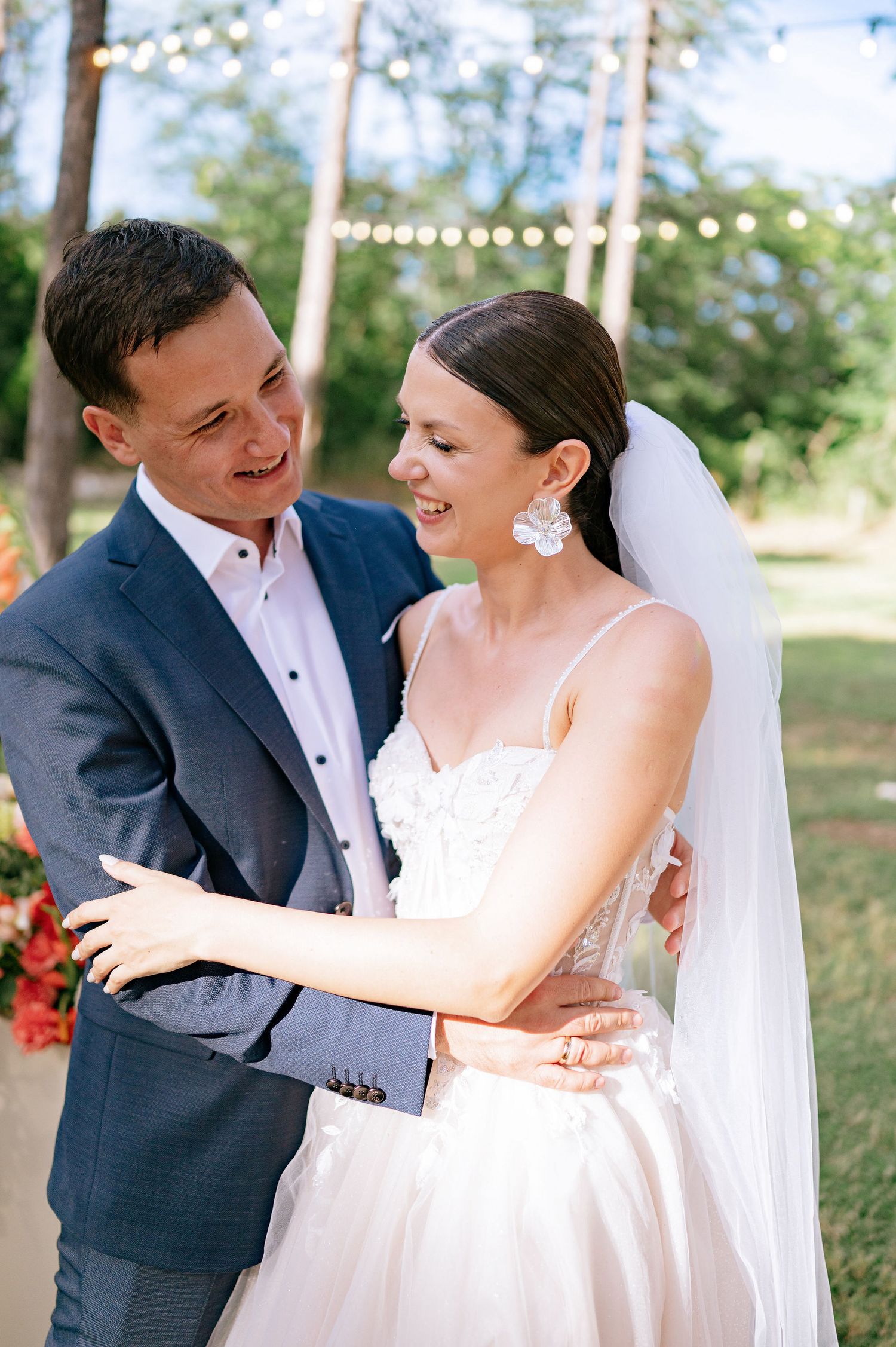 A candid wedding moment showing laughter and joy under string lights in a forest setting.