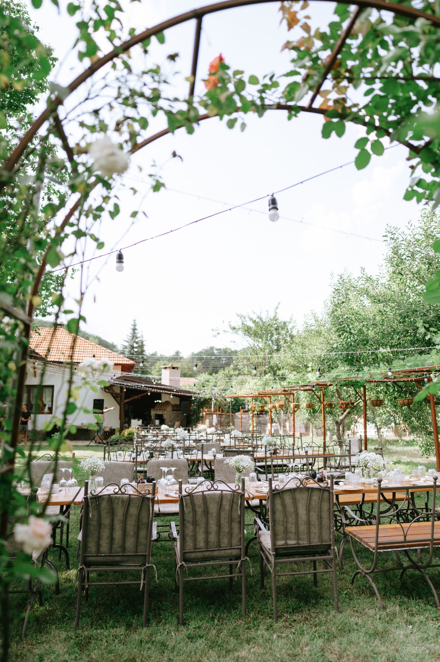 Outdoor wedding venue with string lights and rustic metal chairs arranged under arched pergolas.