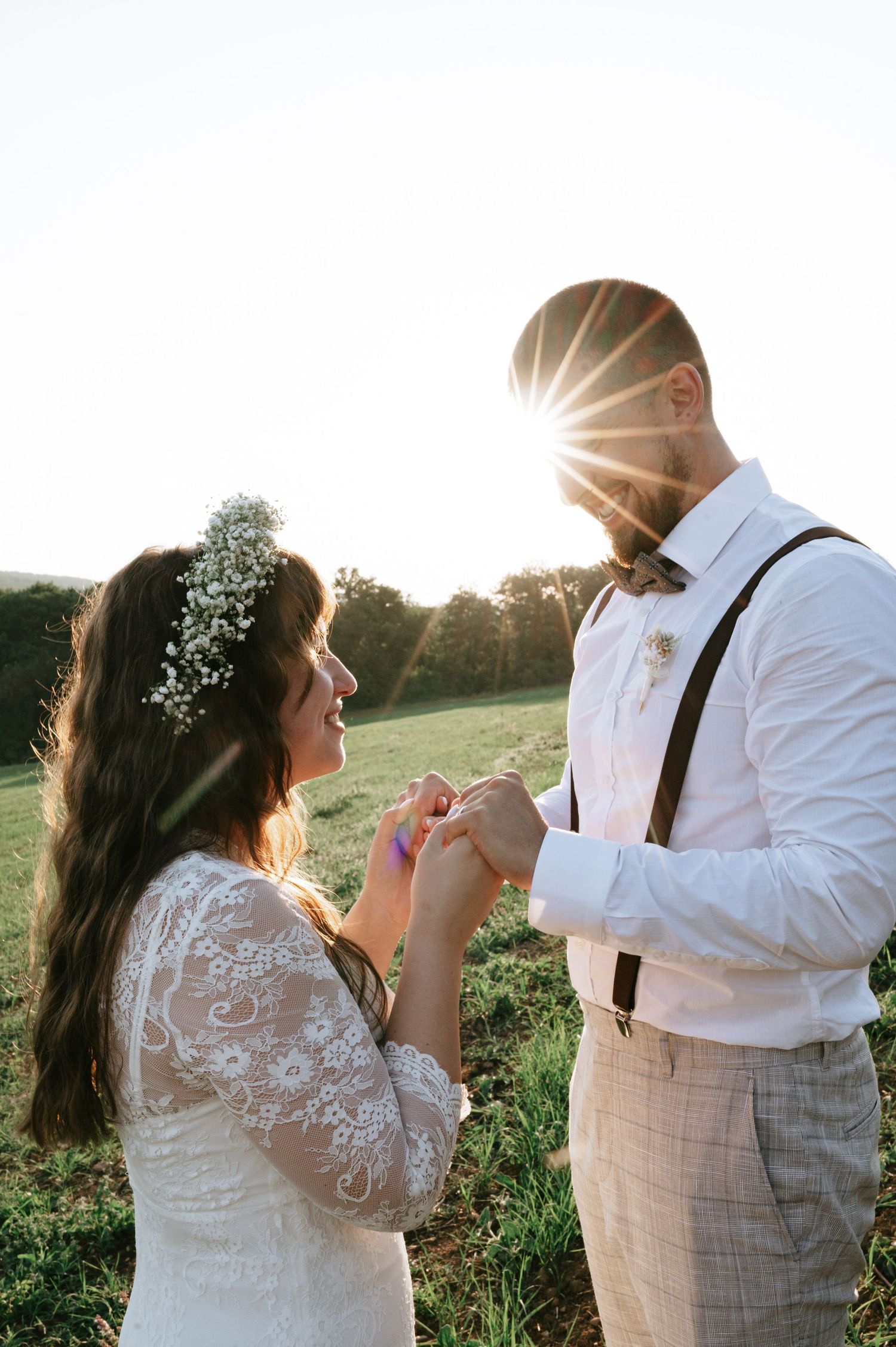 A couple in wedding attire dances together in a sunlit meadow during golden hour.