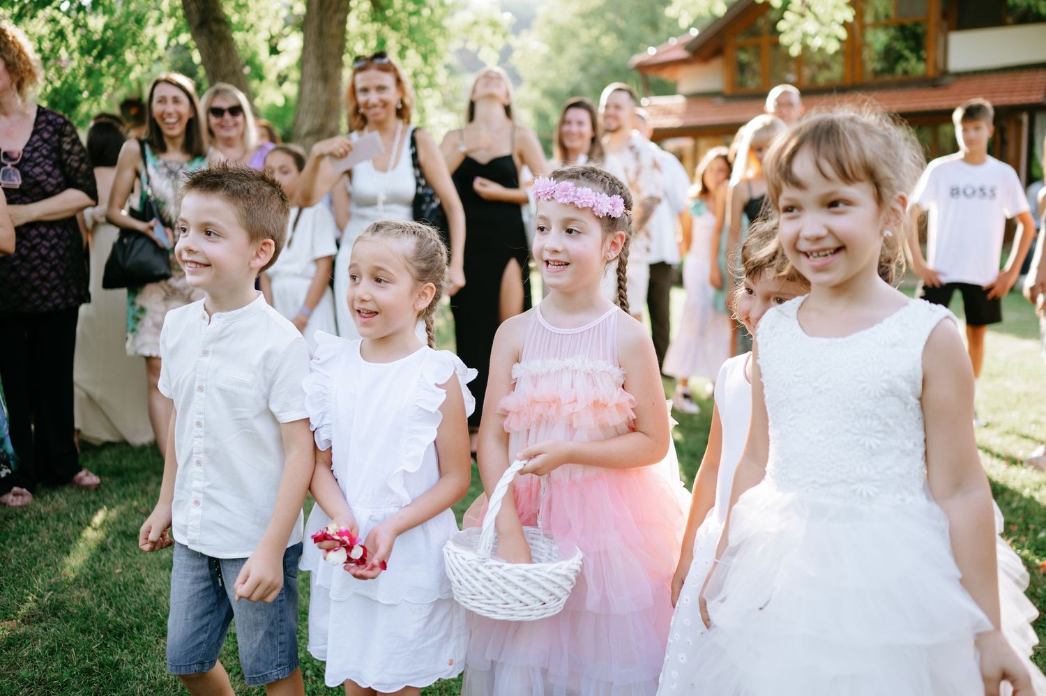 Young children dressed in formal attire carrying flower baskets at an outdoor wedding event.