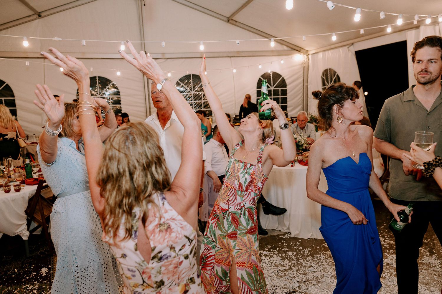Lively dance floor filled with wedding guests celebrating under tent lighting.