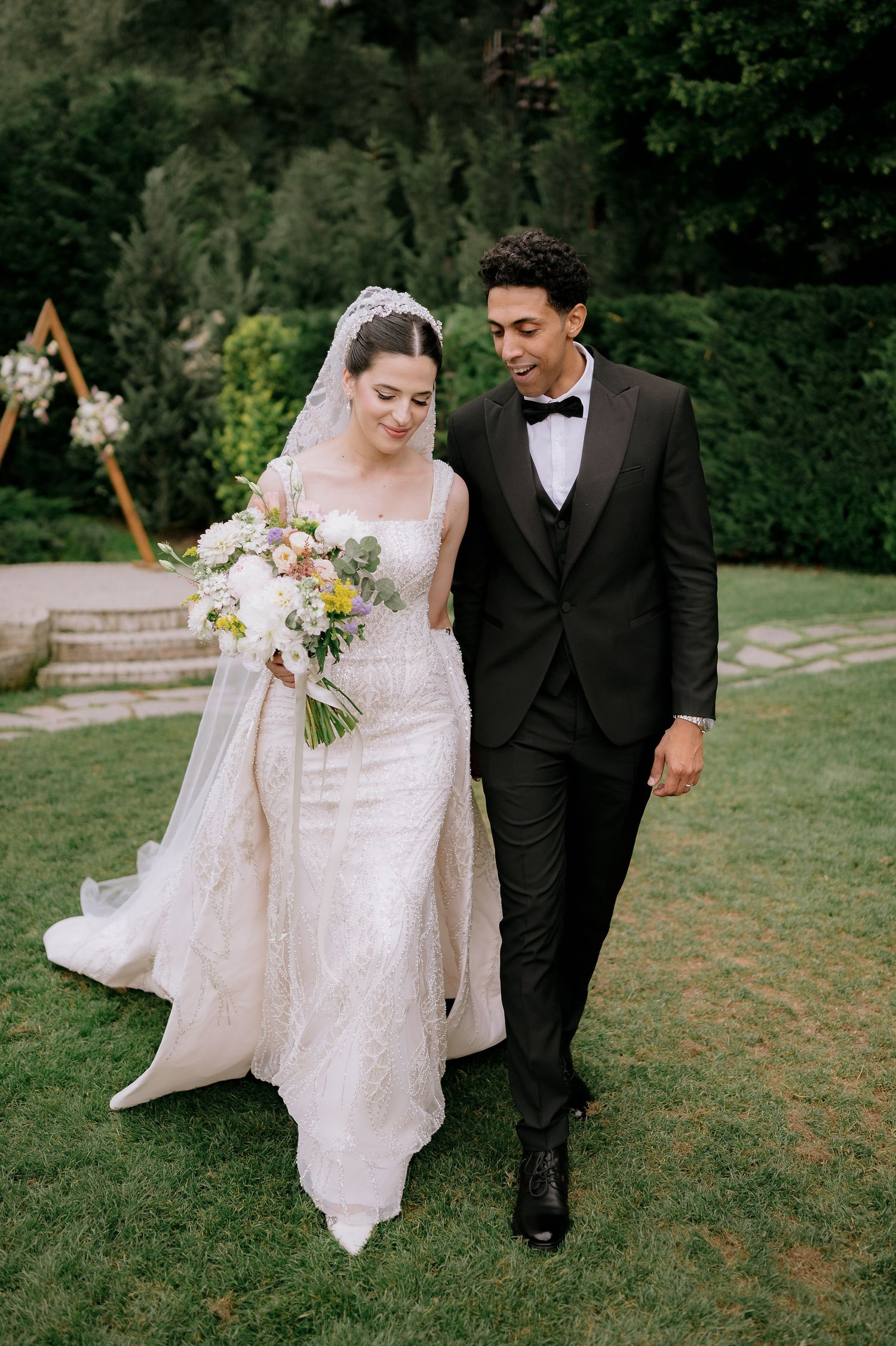 A couple walking hand in hand outdoors, with the bride's white dress flowing in the breeze.
