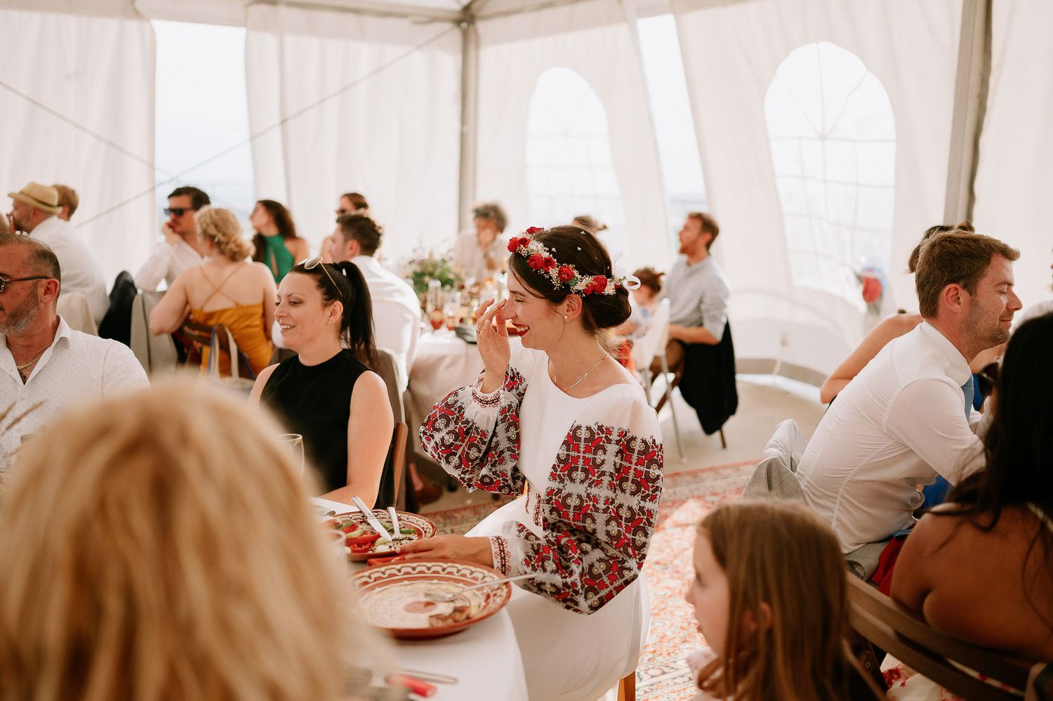 Wedding reception guests seated at long tables under a white tent.
