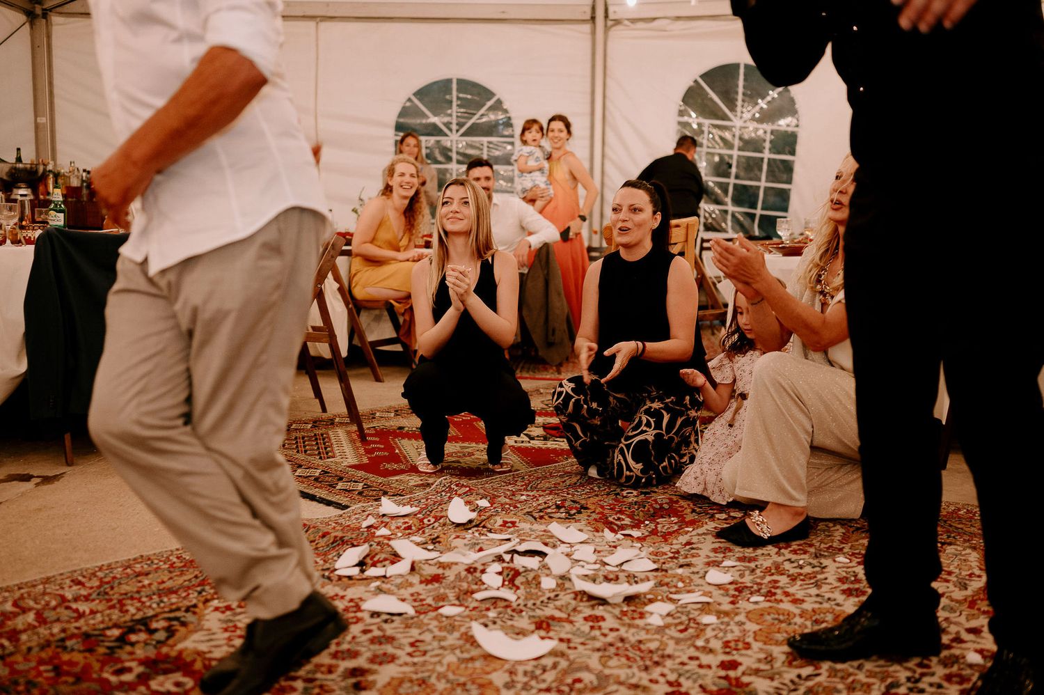 Wedding guests dancing on a patterned carpet under a reception tent.