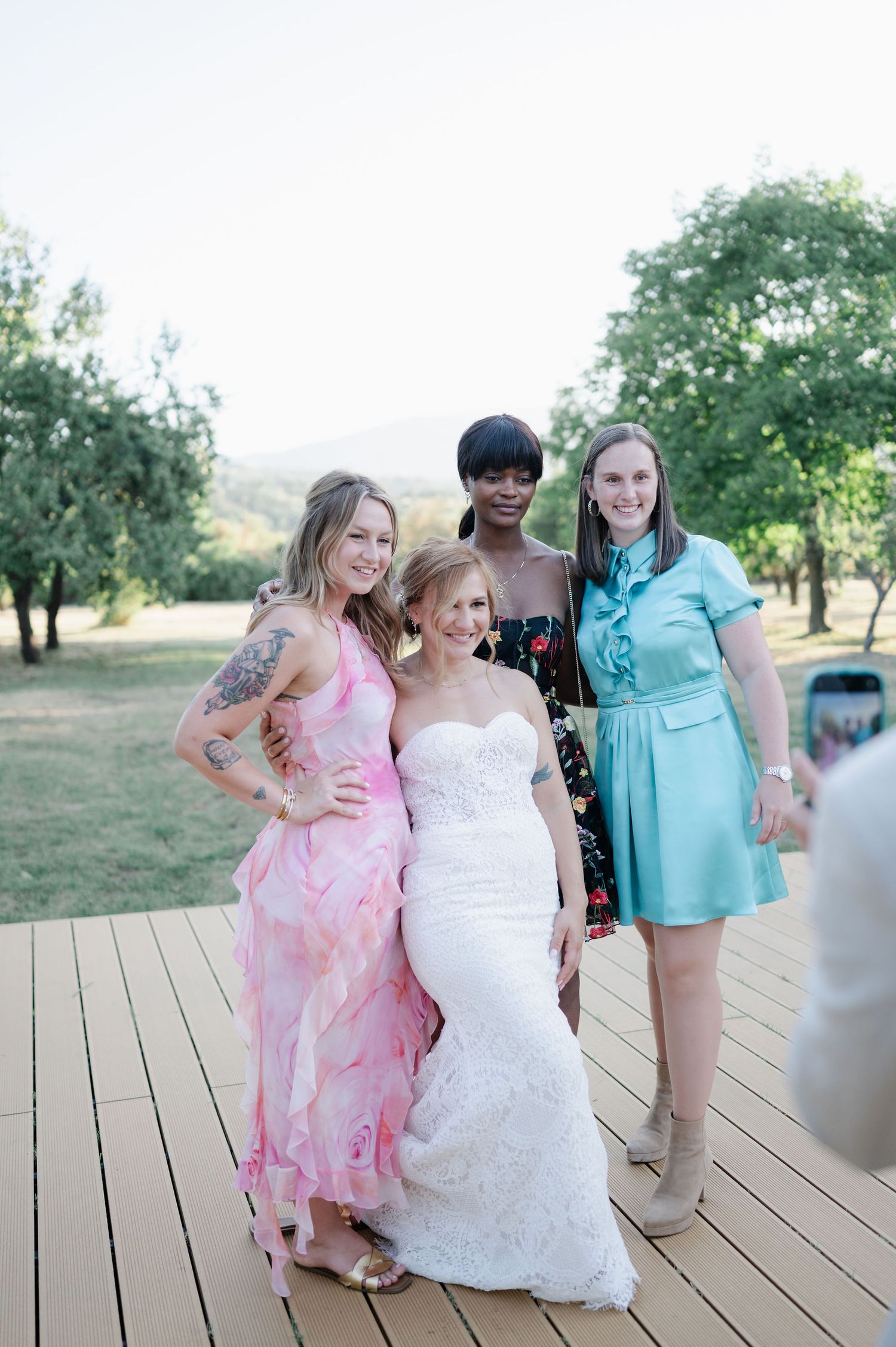 Wedding party laughing together on wooden deck in pink and turquoise dresses.