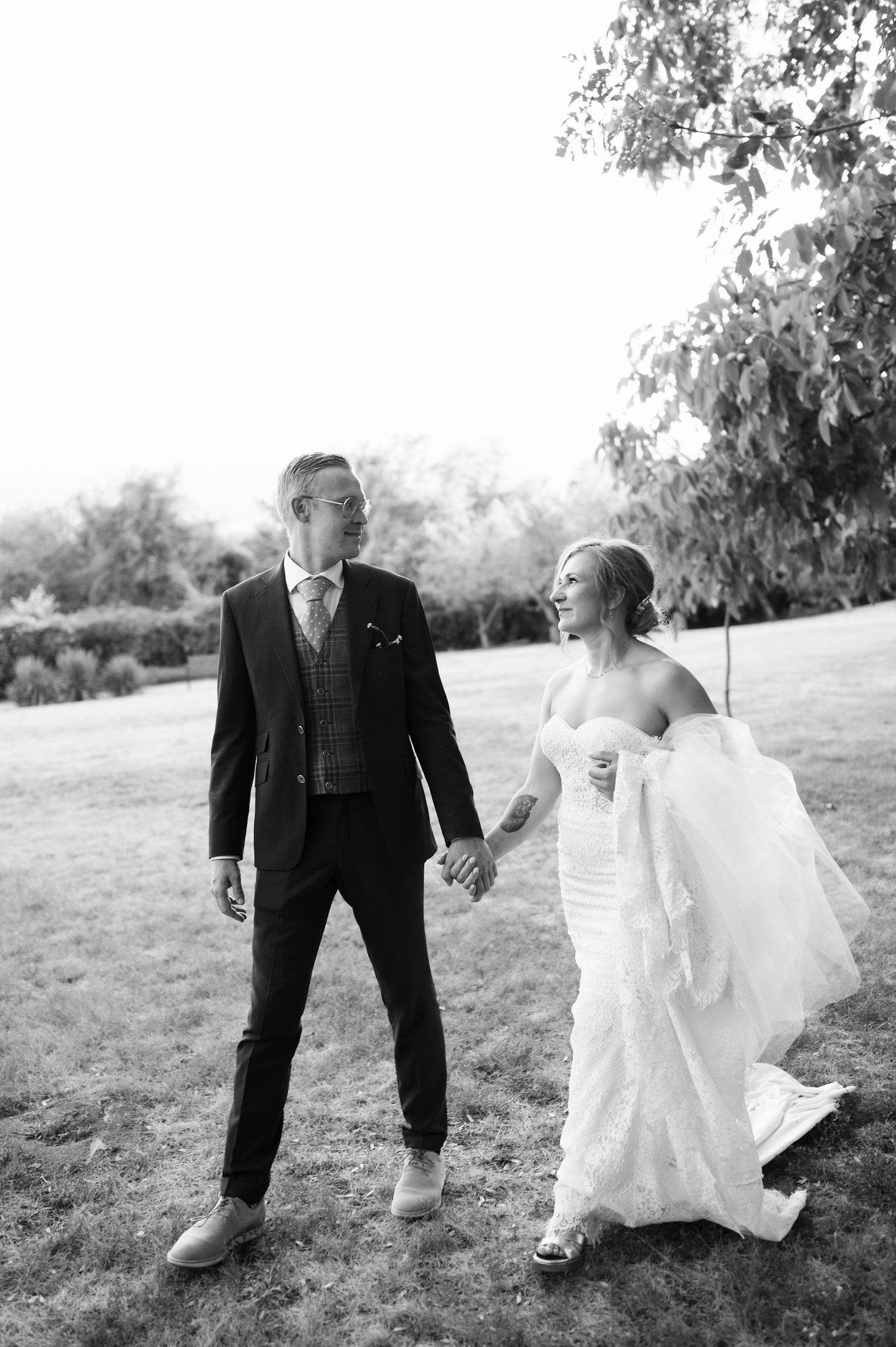 A couple holds hands while walking through a grassy outdoor setting.