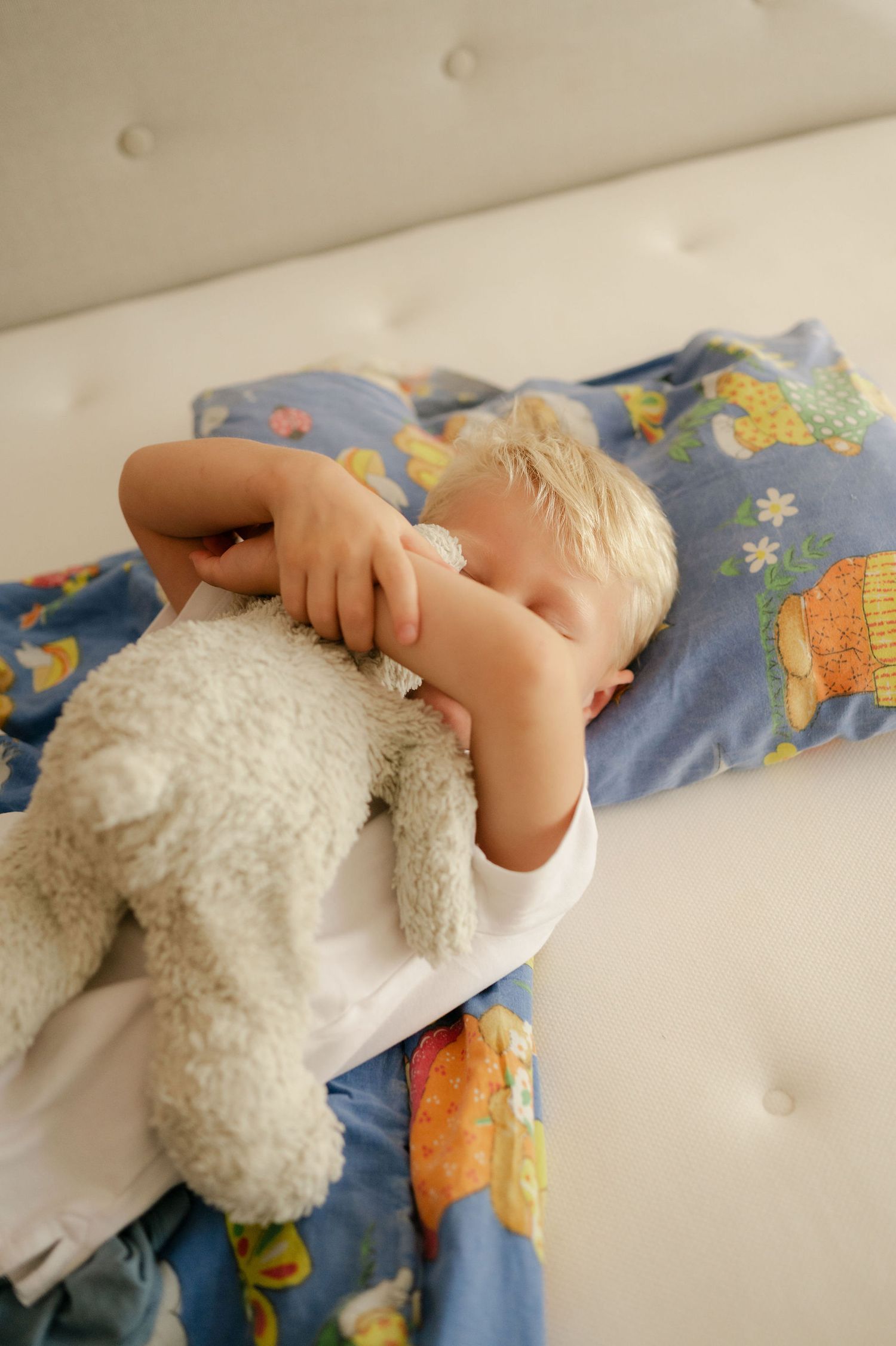A small child in blue pajamas holds a white plush toy while lying on bedding.