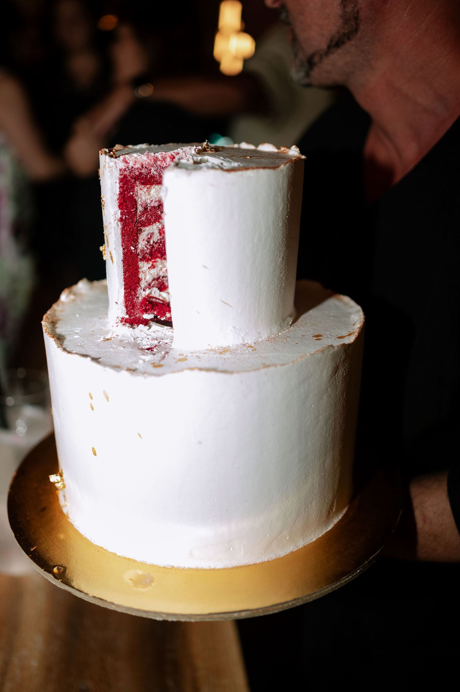 Two-tiered white wedding cake with red velvet interior on a gold cake board.