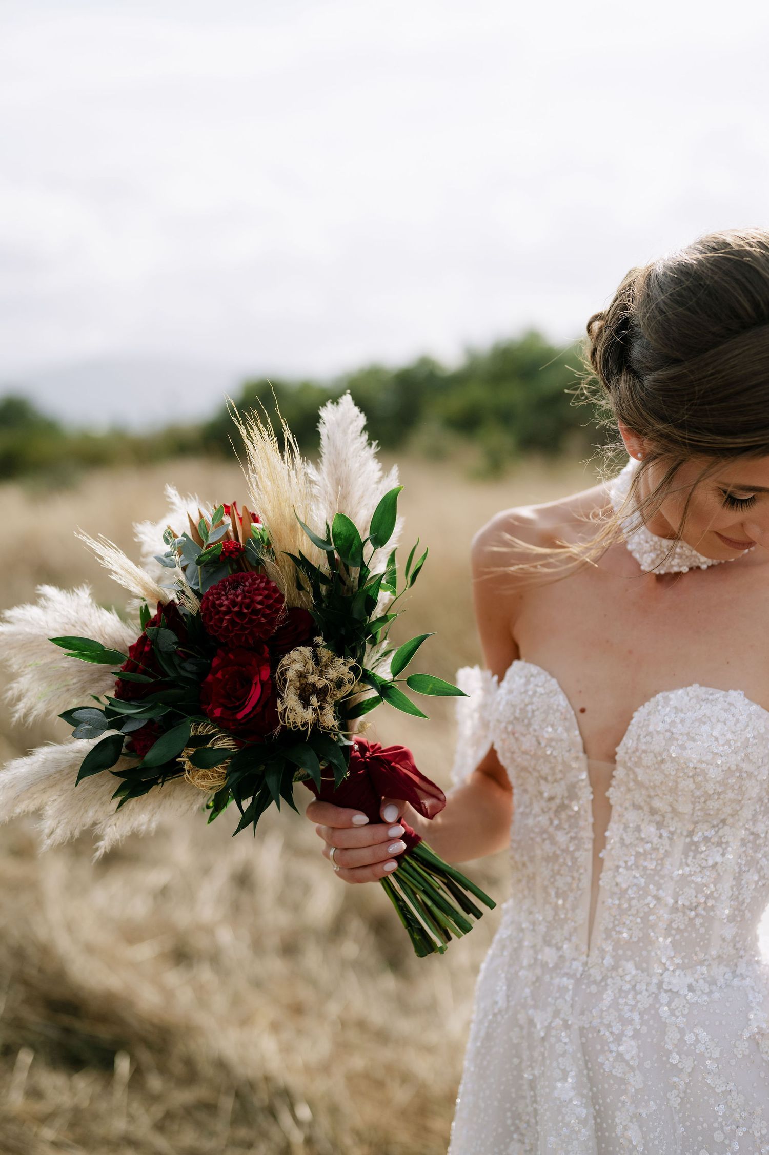 Close-up of bridal bouquet featuring deep red flowers against a white wedding gown.