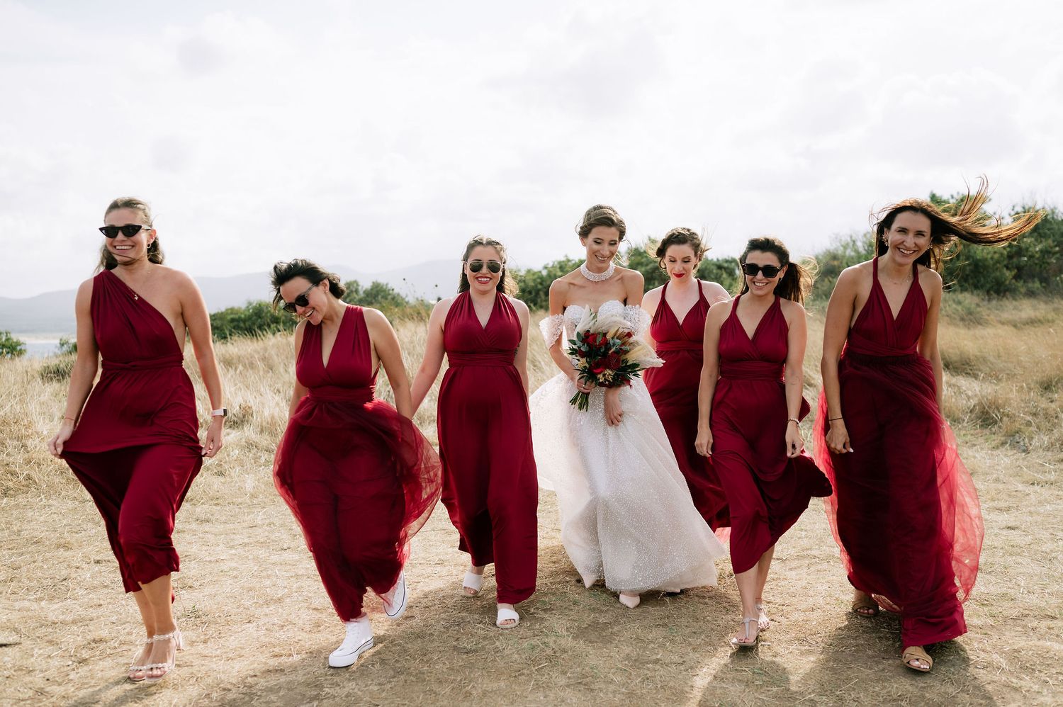 Bridal party in coordinated burgundy dresses poses on natural terrain.