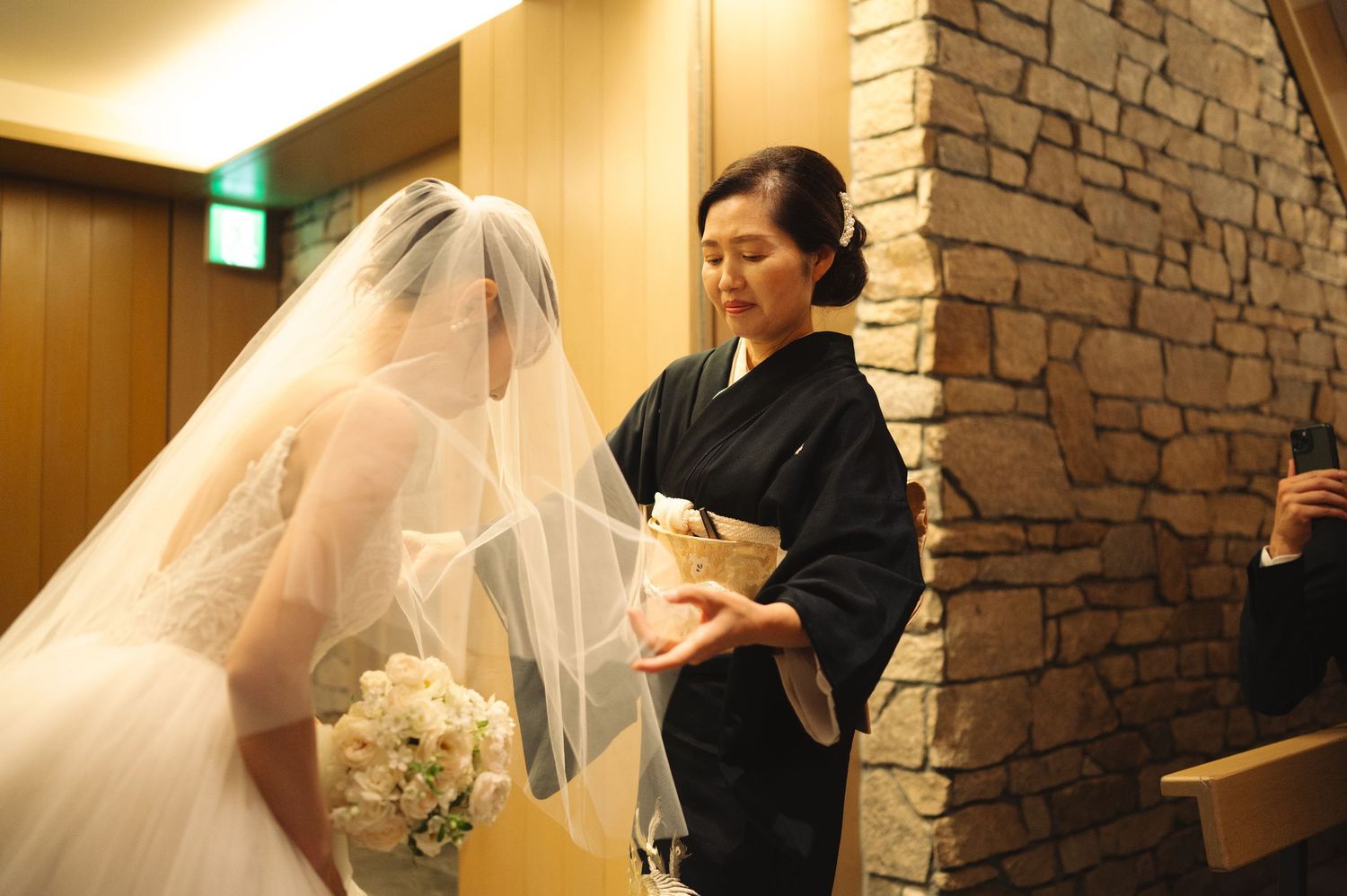 Wedding dress fitting scene showing final adjustments being made to a flowing white gown and veil.