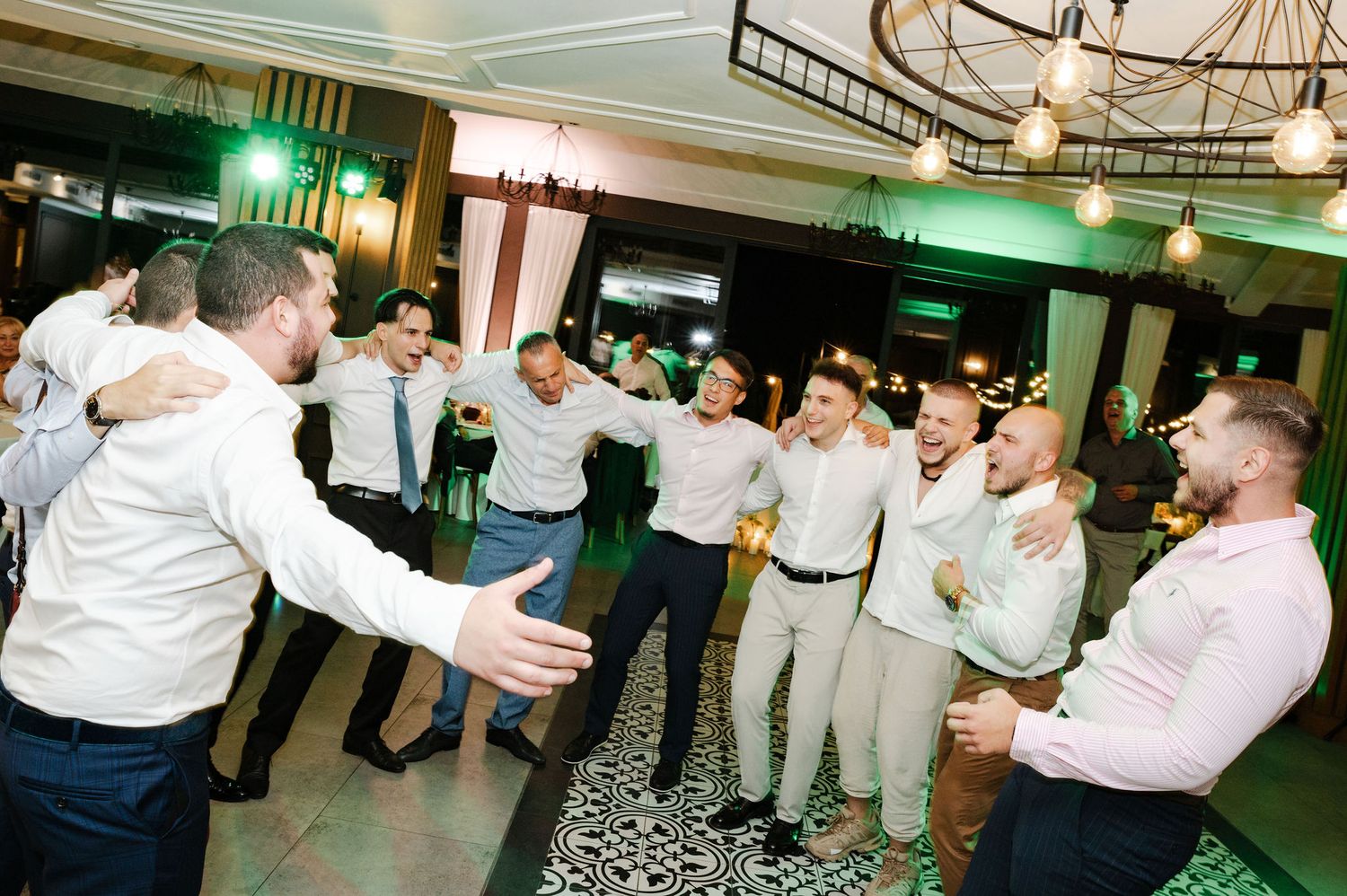 Wedding guests dancing in formation with arms outstretched on a patterned carpet.