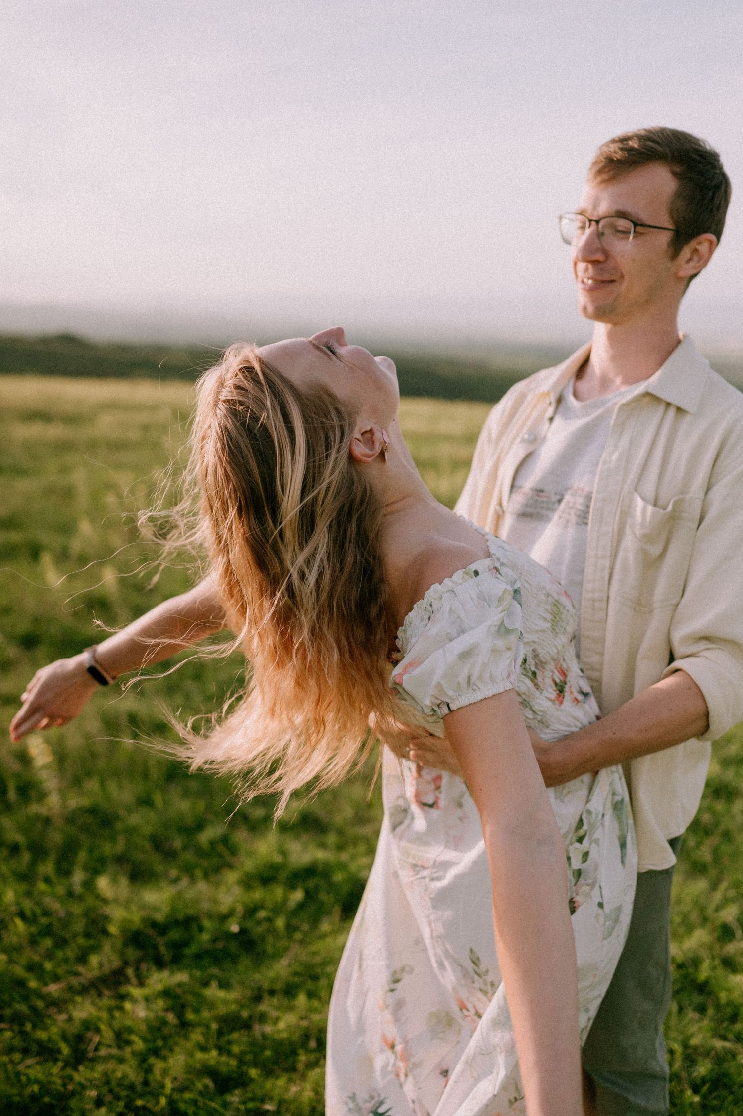 Romantic couple dancing and twirling together in a golden field at sunset.