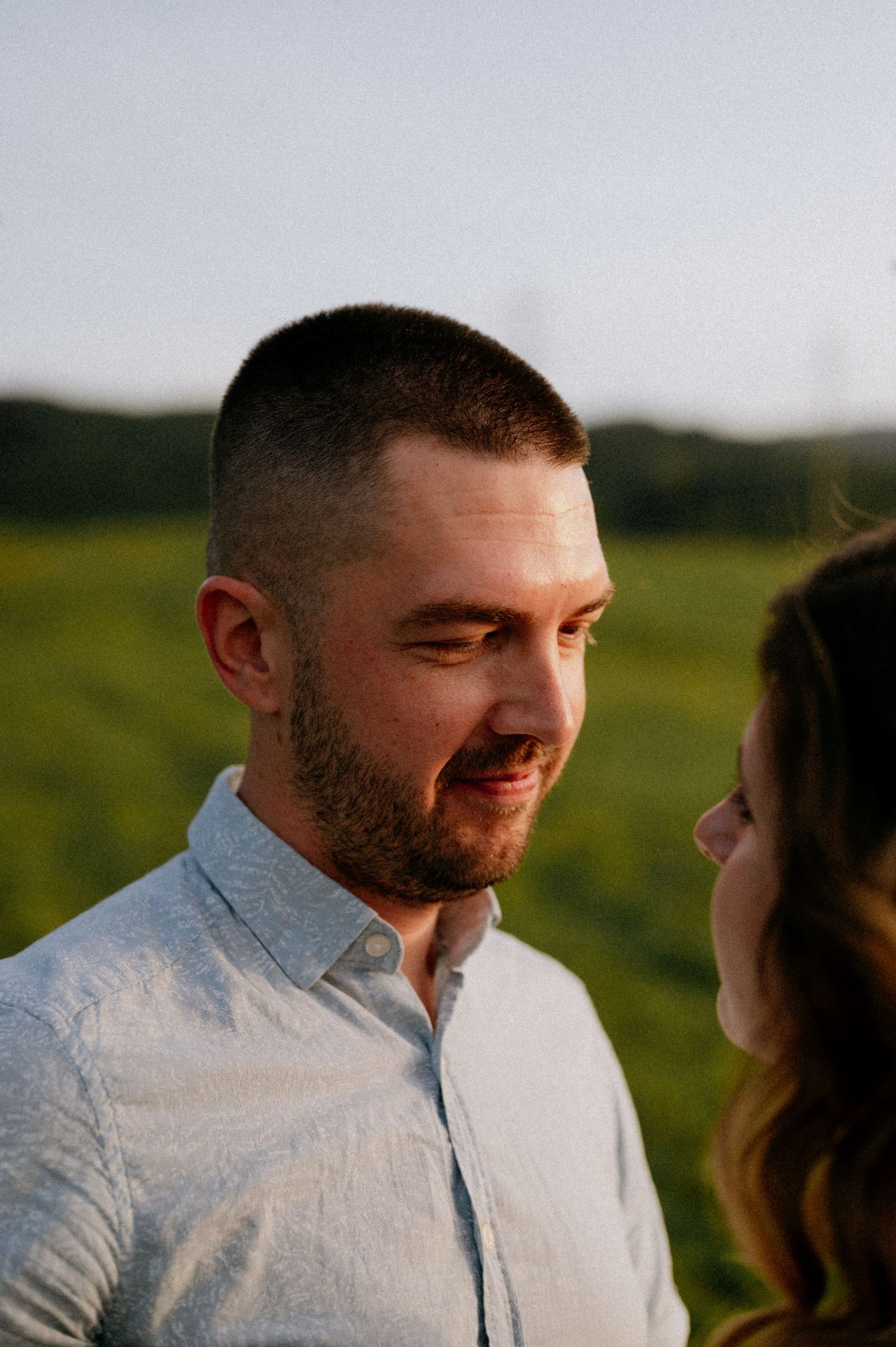 A couple shares a tender moment while smiling at each other in the warm evening light.
