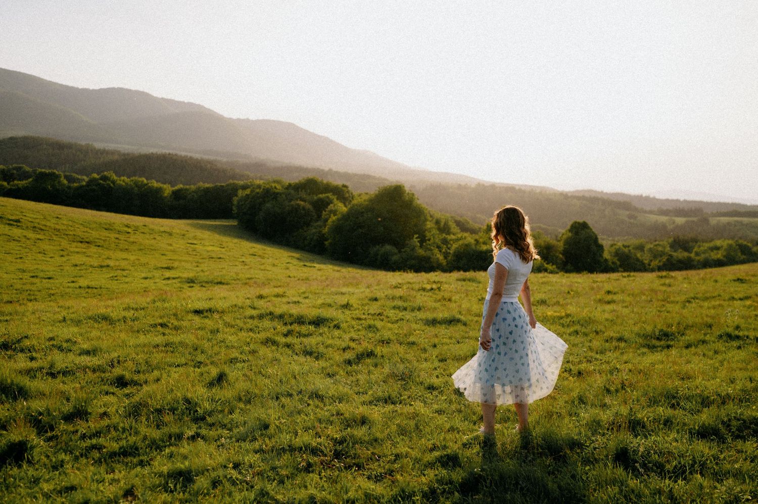 Someone dances joyfully in a white dress on a scenic hilltop during golden hour.