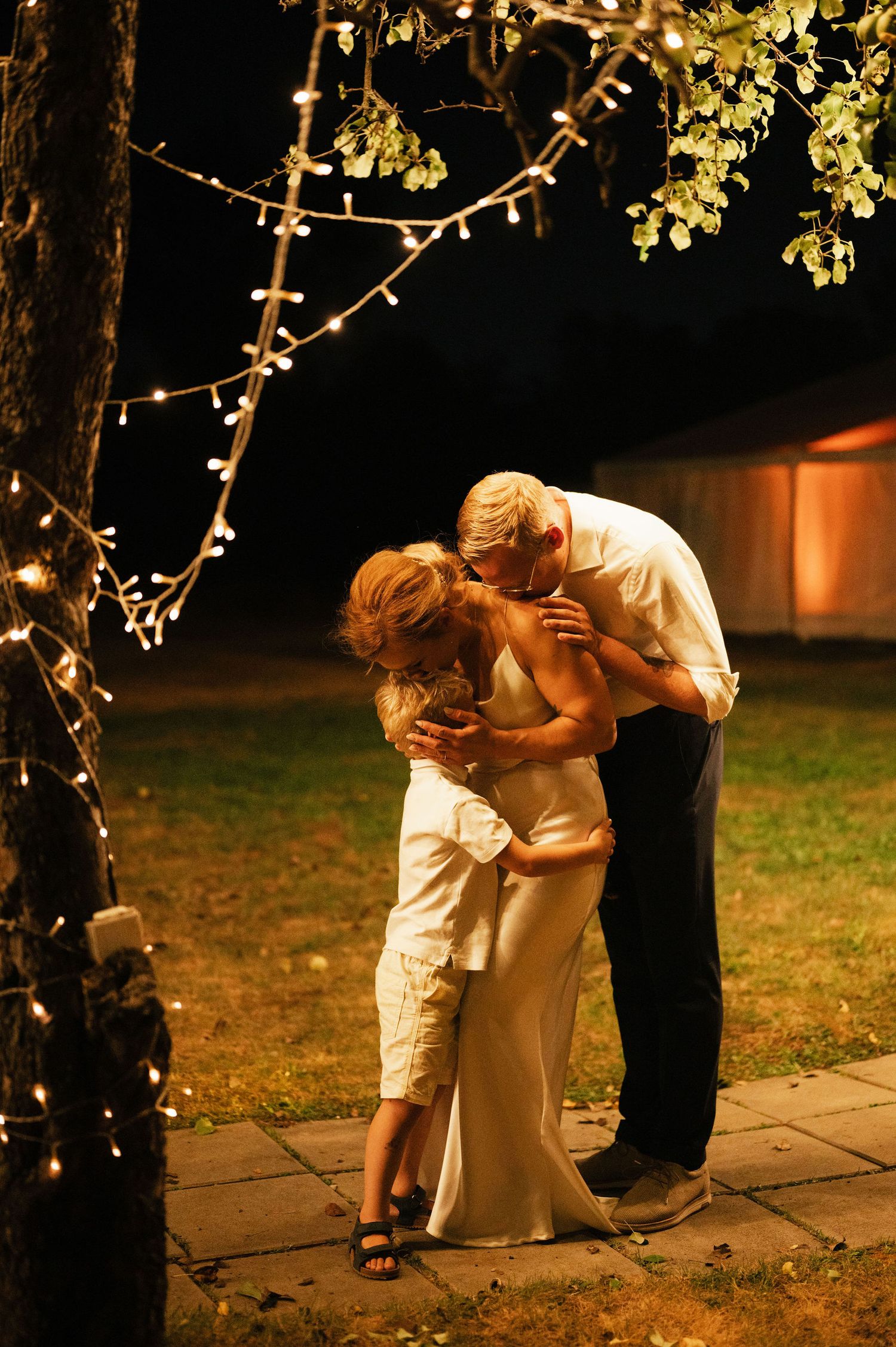 A romantic evening embrace under twinkling string lights in a garden setting.