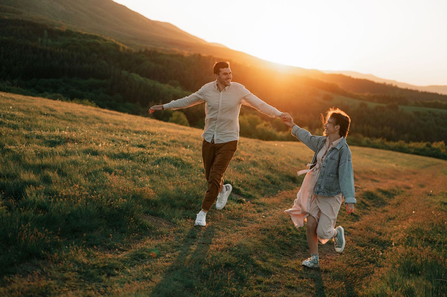 A couple dances together in a golden meadow at sunset, their silhouettes casting long shadows across the grass.