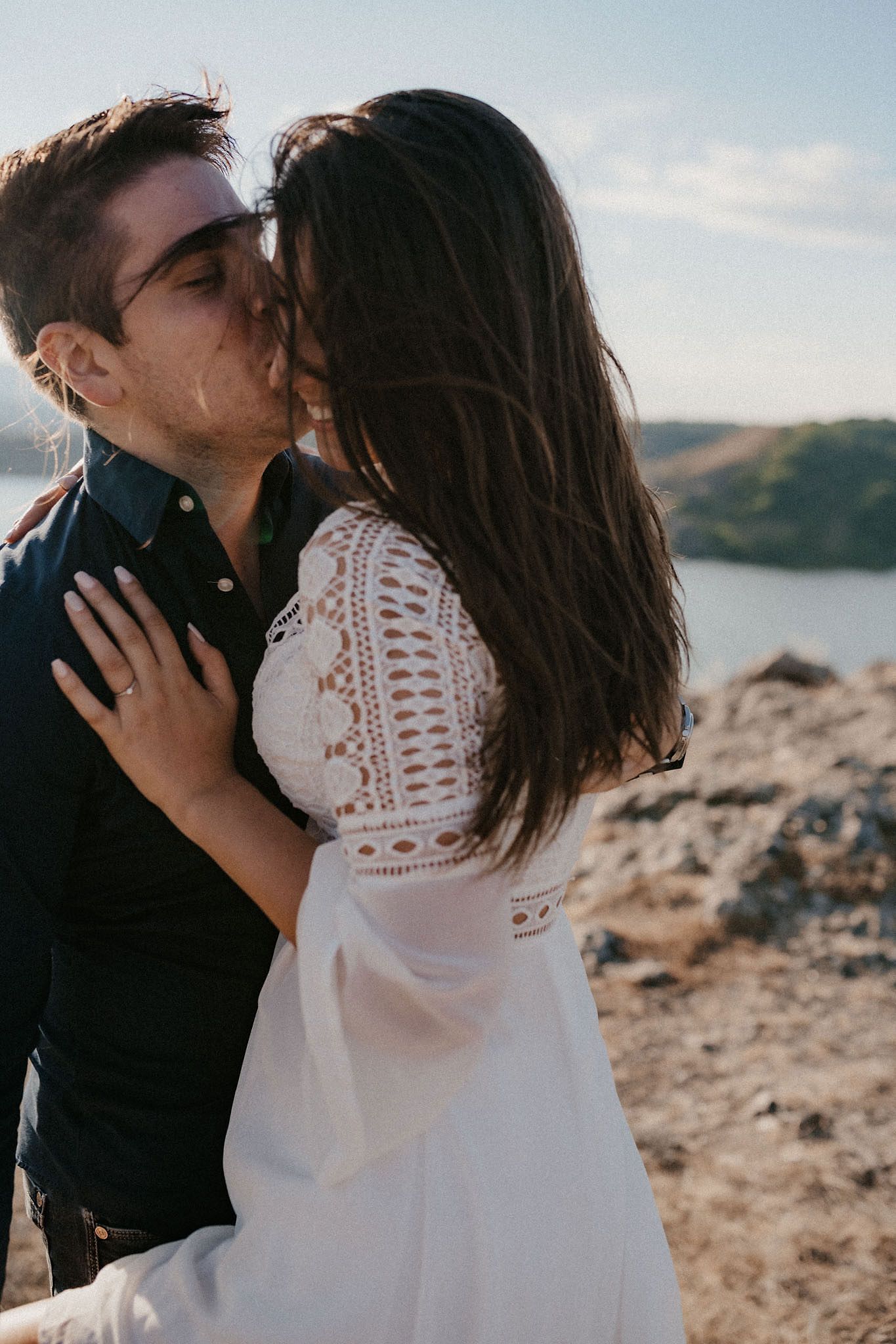 Intimate couple in white lace and black clothing sharing tender moments against a mountain backdrop.