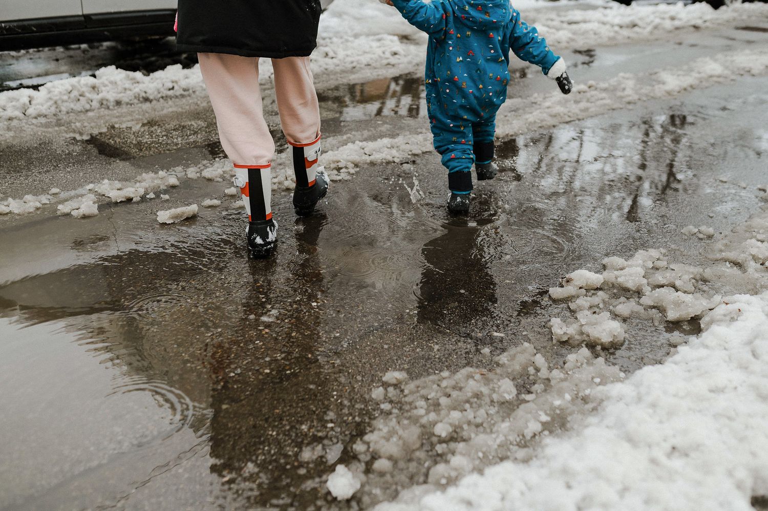 Two people in winter boots splash through melted snow puddles on a slushy winter street.