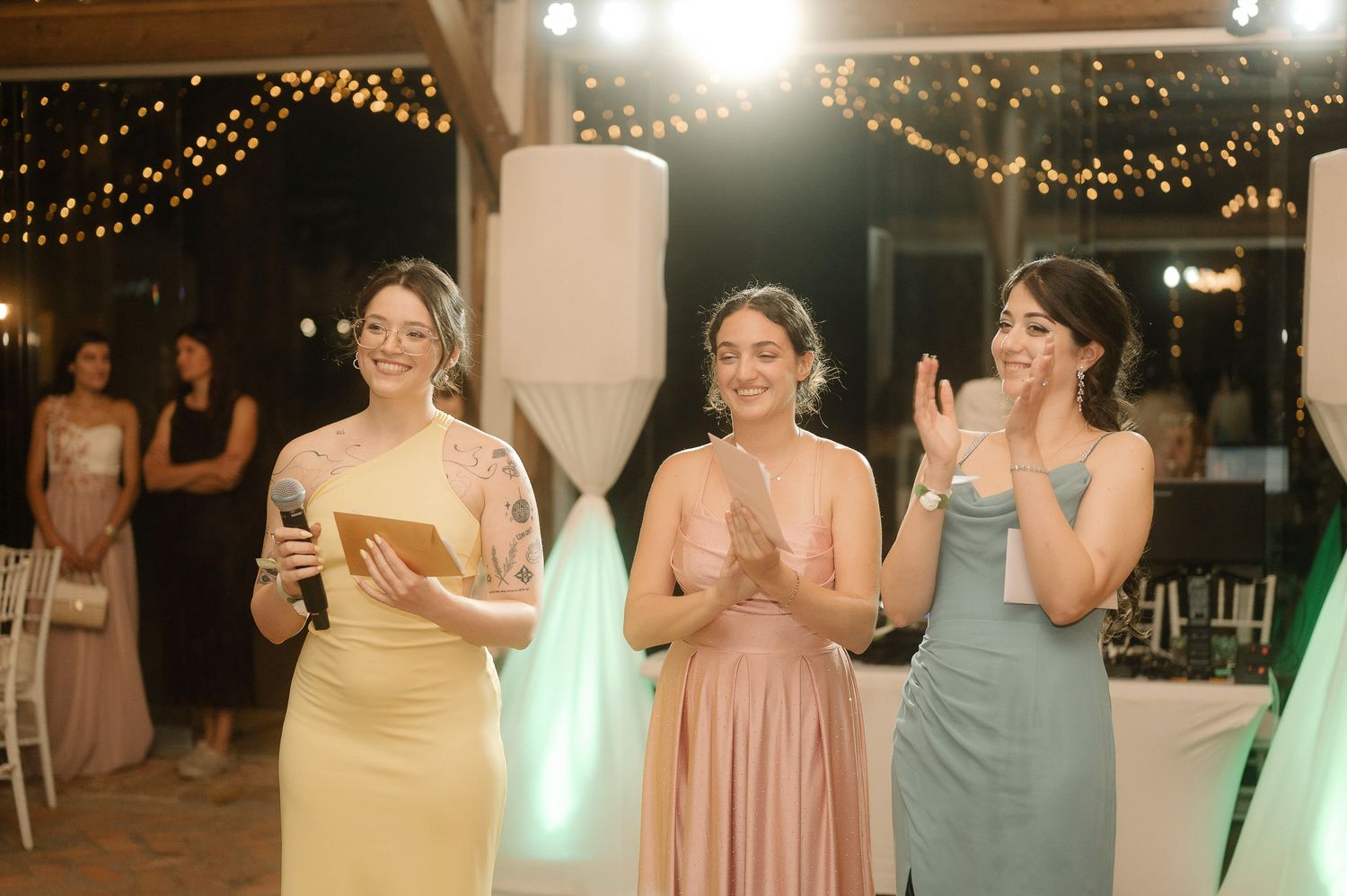 A wedding reception scene with bridesmaids in pastel dresses dancing under string lights and decorative lighting.