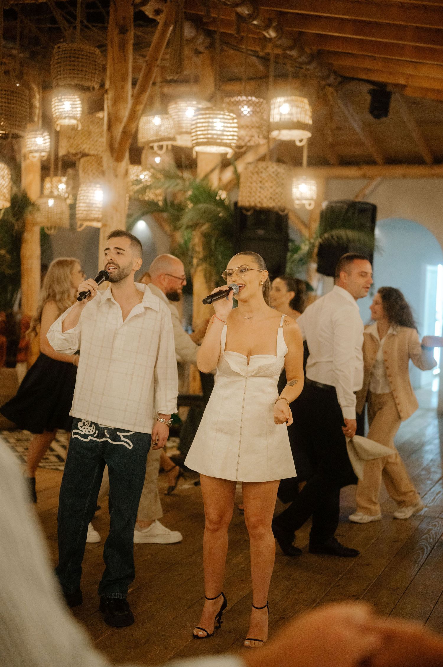 Wedding guests dancing together on a rustic wooden dance floor illuminated by warm overhead lighting at a reception.