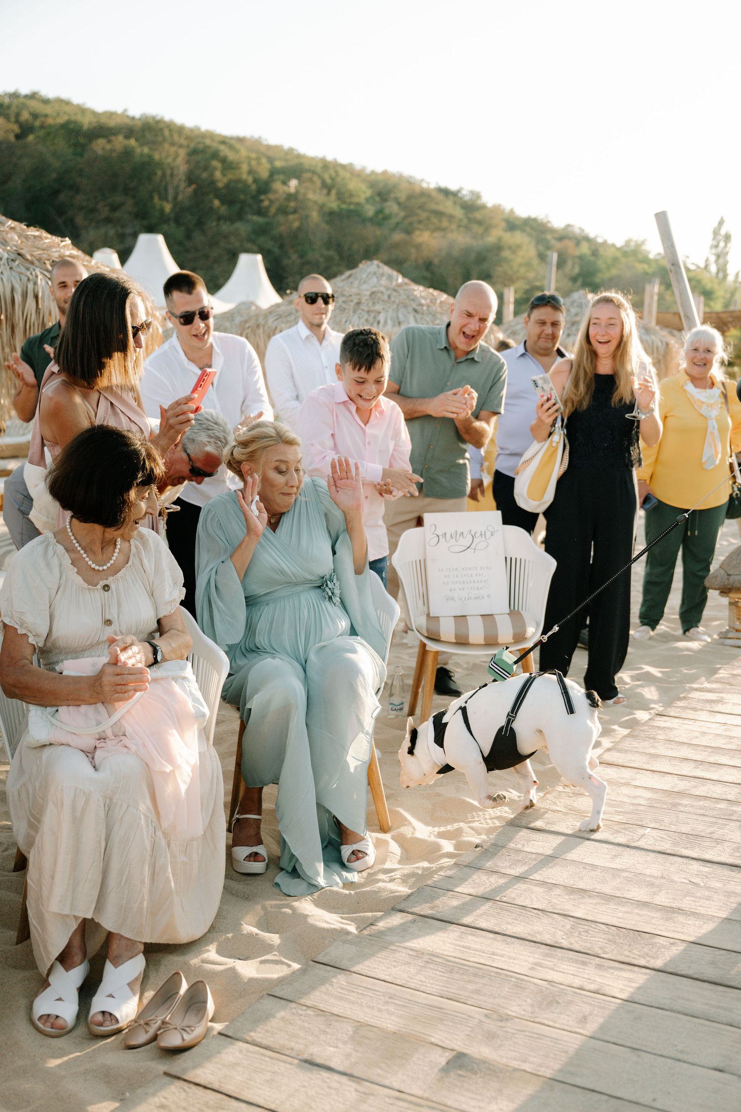 Wedding guests sitting in white chairs on a wooden deck during sunset celebrations.