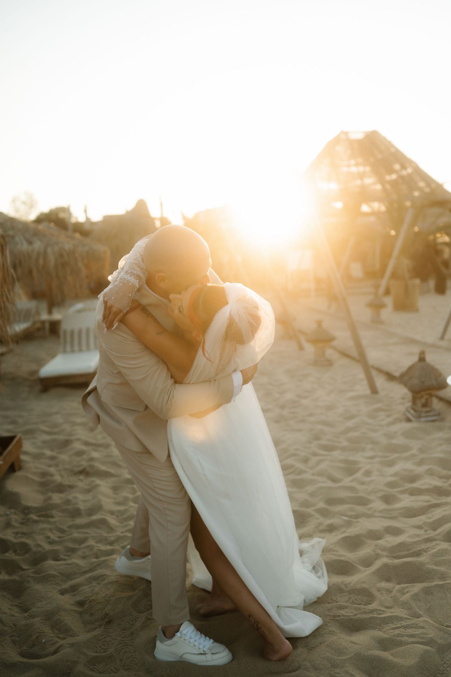 A romantic sunset beach photo series showing a couple in white and beige embracing on the sandy shore.