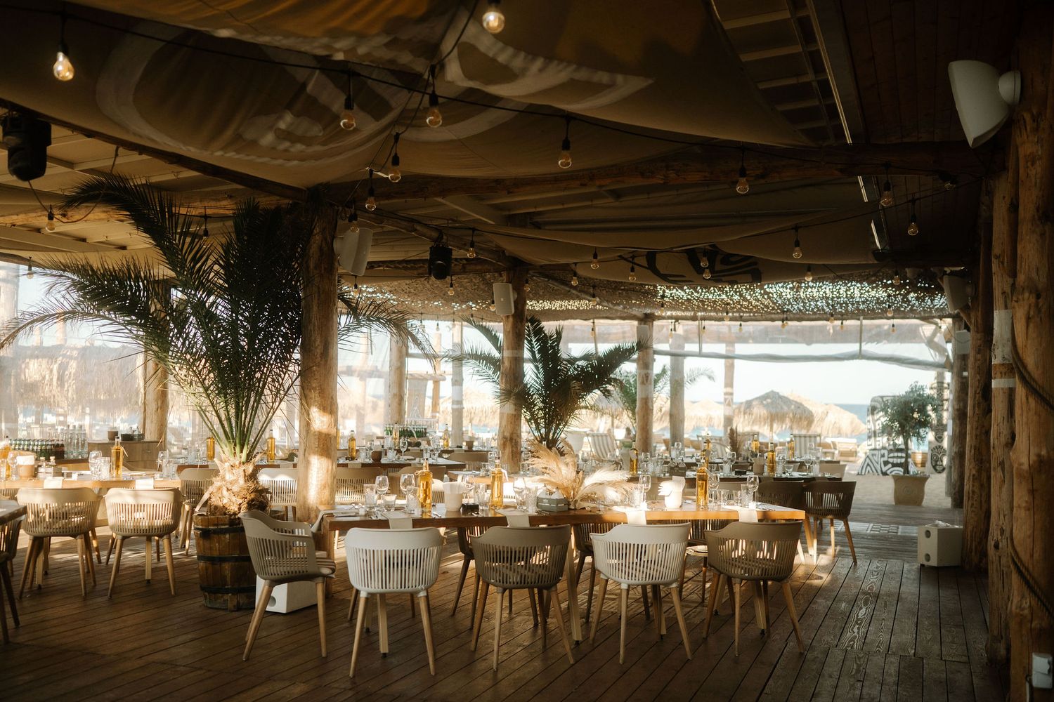 Rustic wooden restaurant interior with warm lighting, rattan chairs, and multiple dining areas creating a cozy atmosphere.