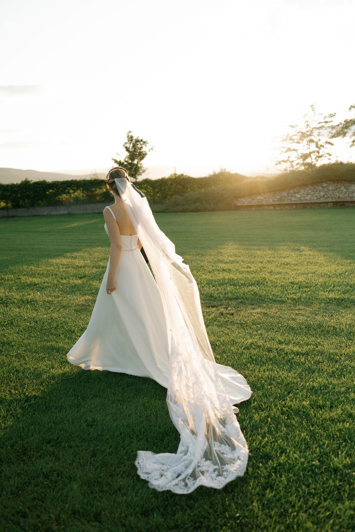 A flowing white wedding dress billows in the wind as a figure twirls on a grassy field at sunset.