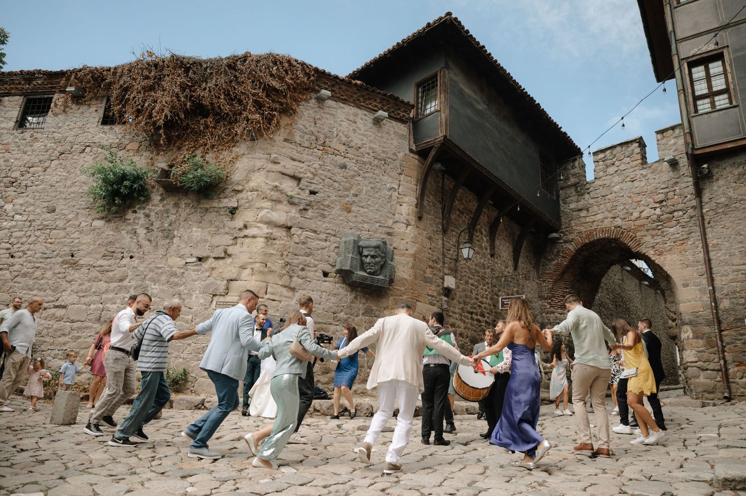 People running through a narrow stone alleyway in an ancient village during what appears to be a festival or event.