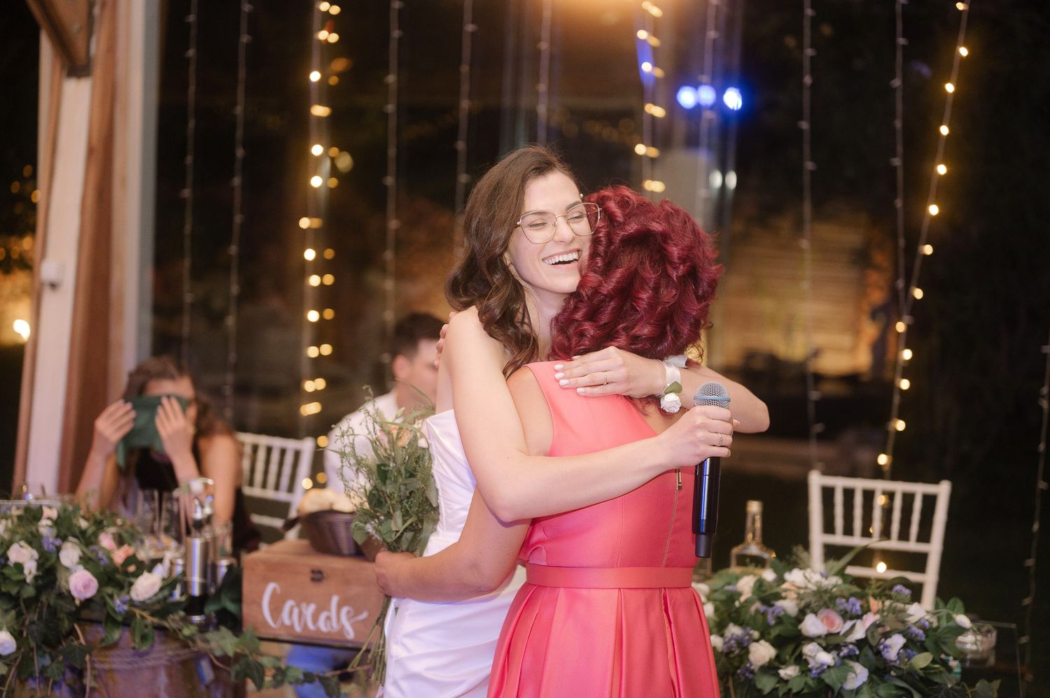 Wedding guests dance and embrace on a dimly lit dance floor surrounded by string lights and floral decorations.