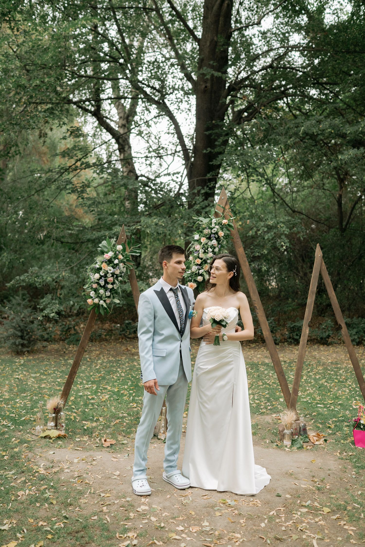 A couple shares a joyful moment at their outdoor woodland wedding ceremony with floral decorations and rustic wooden details.