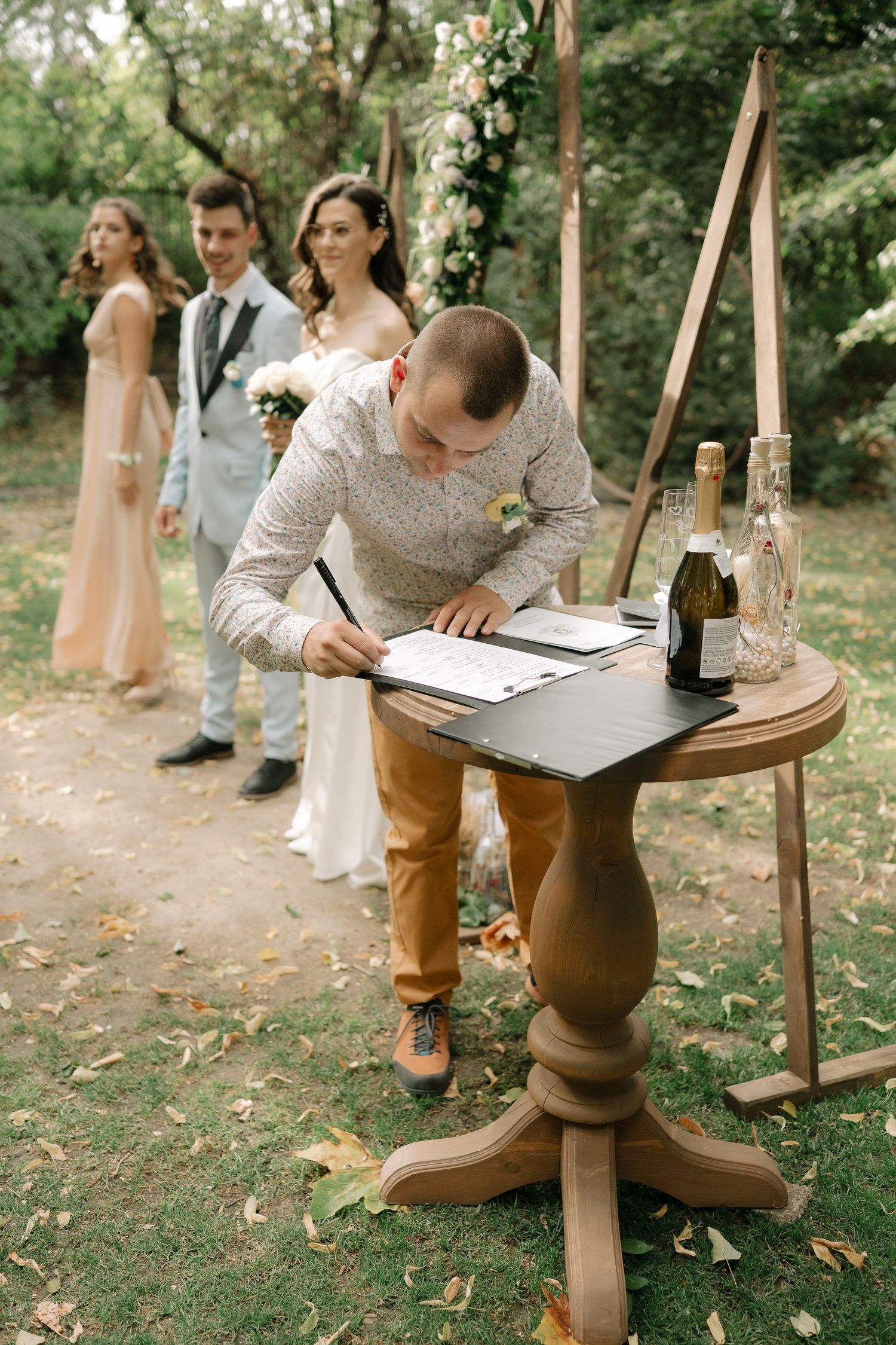 A couple signs their marriage license at a rustic wooden table during an intimate outdoor garden ceremony.