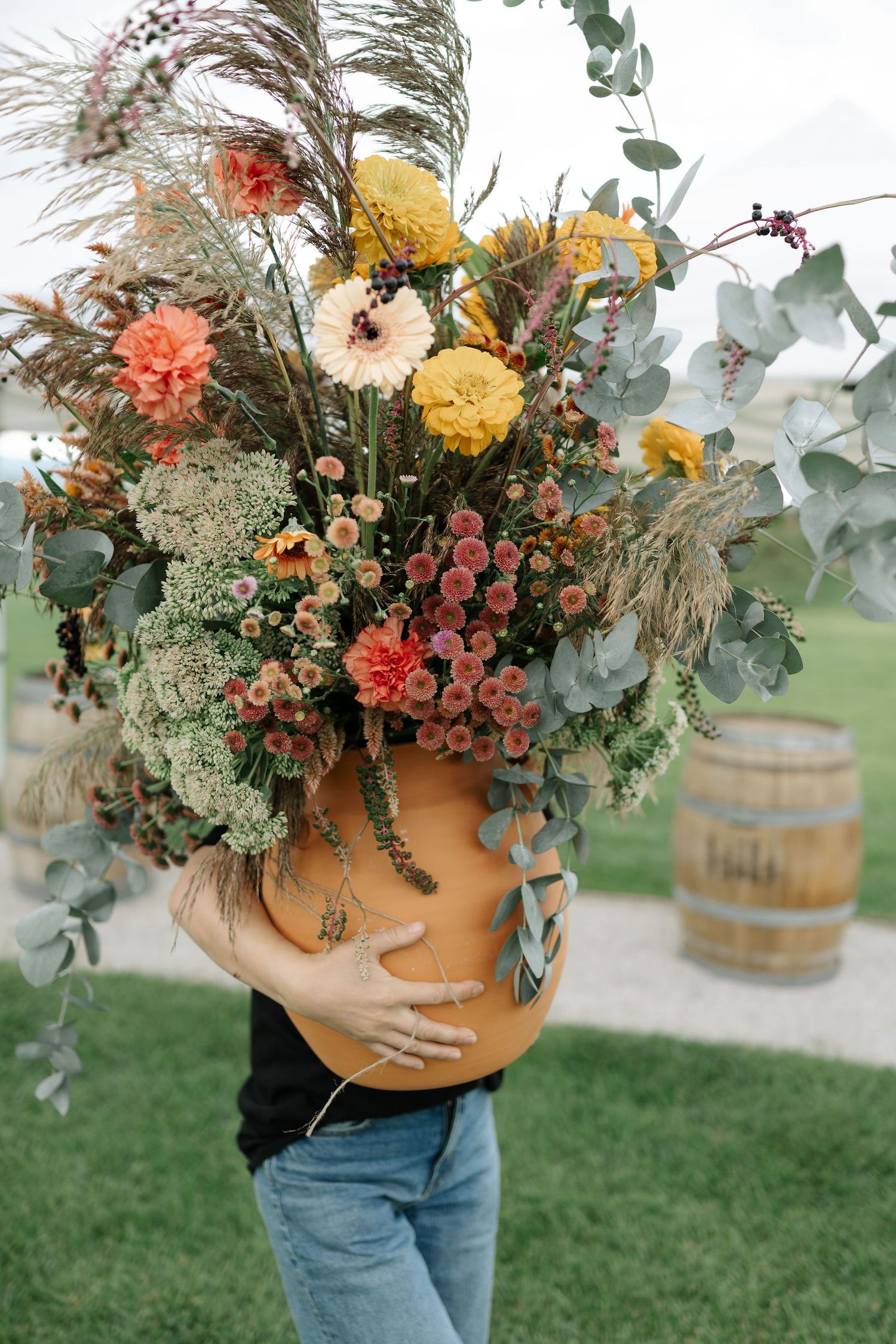Colorful autumn floral arrangement with dried pampas grass and eucalyptus held against blue jeans outdoors.