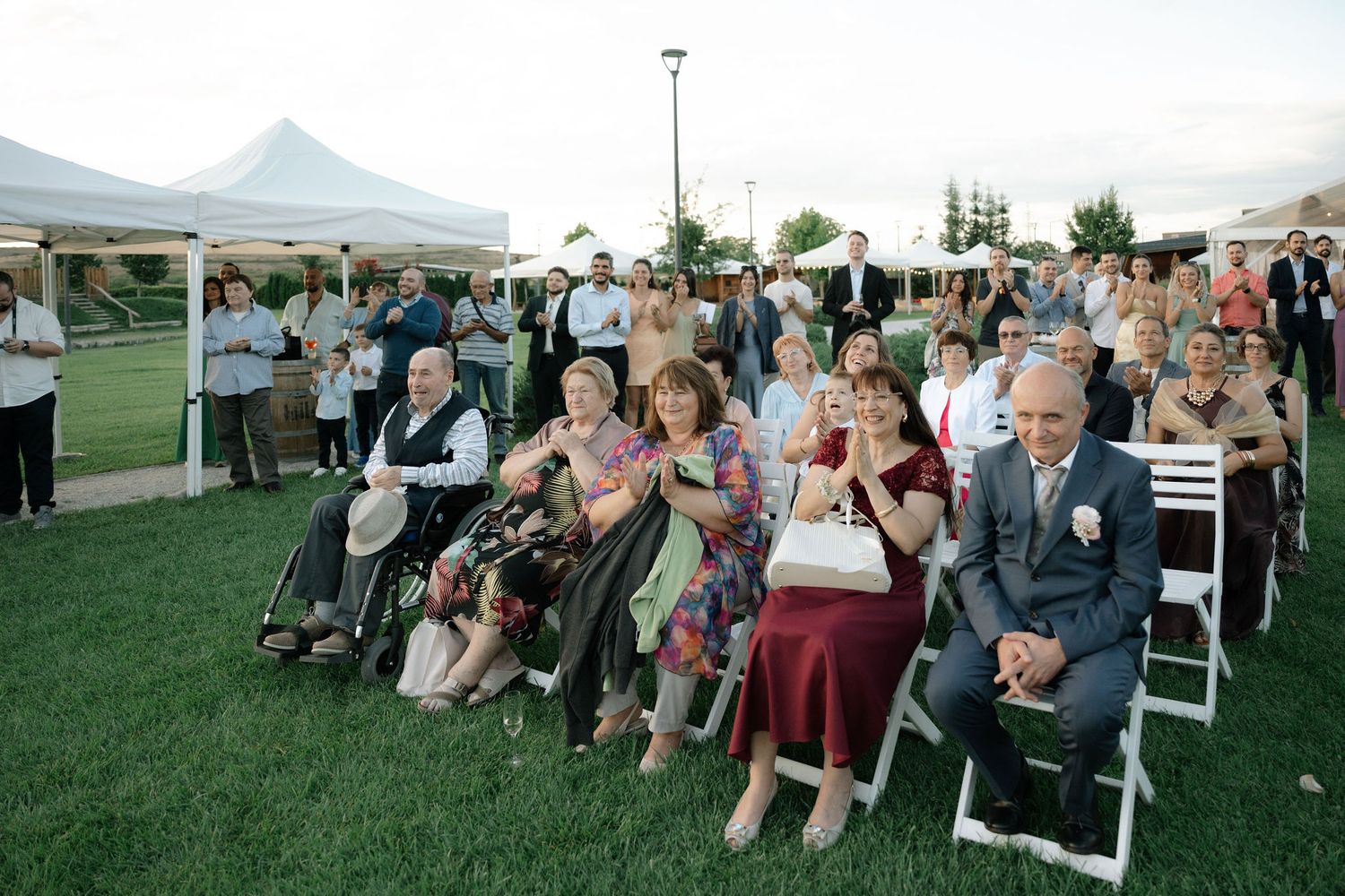 Wedding guests seated in white chairs on a lush green lawn with mountain views in the background during an outdoor ceremony.
