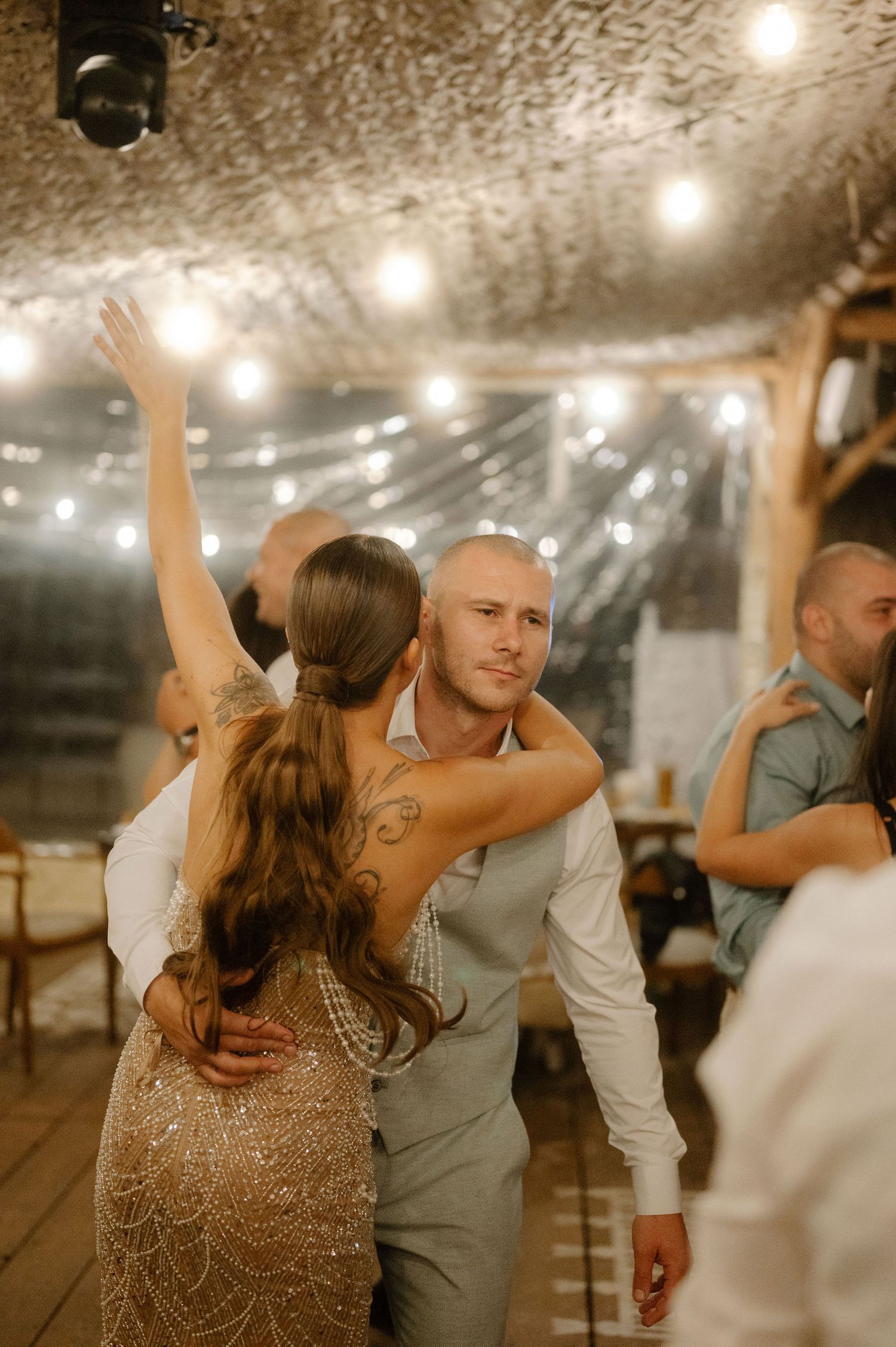 A couple shares an intimate dance moment under warm string lights at their wedding reception.