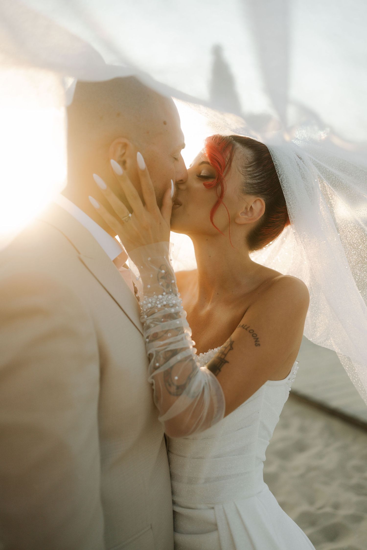 A romantic beach wedding scene showing a couple embracing under a flowing white veil during golden hour.